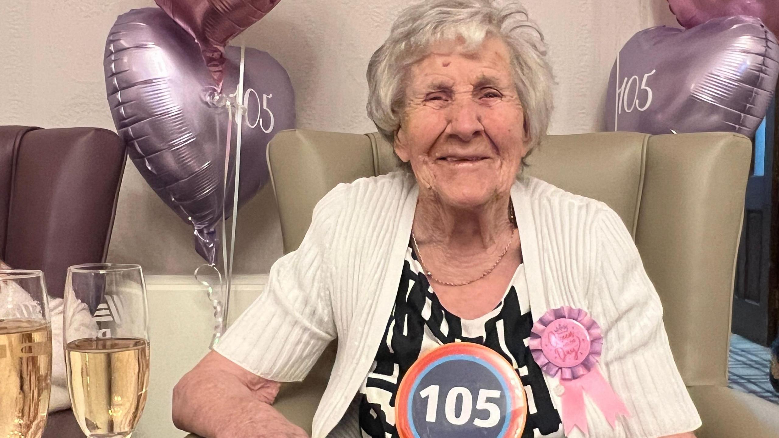 Hilda Jackson with purple 105 heart balloons and champagne glasses and wearing a 105 birthday badge at her 105th birthday rave in Derbyshire