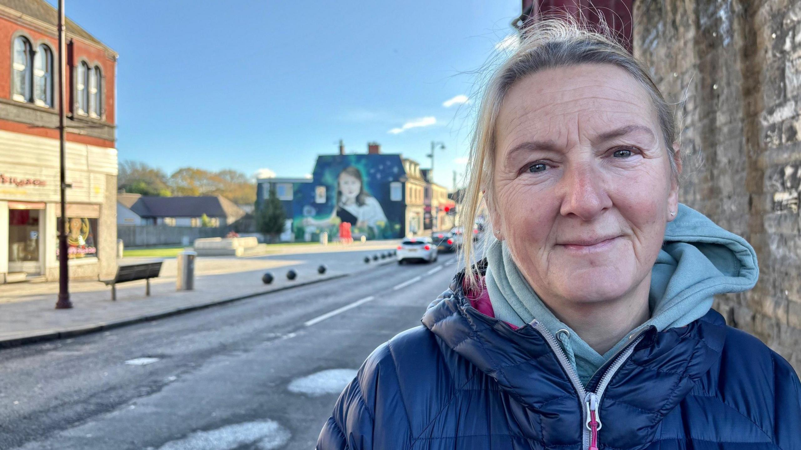 Kirsty is wearing a hooded jacket. She has blonde hair which is tied back.