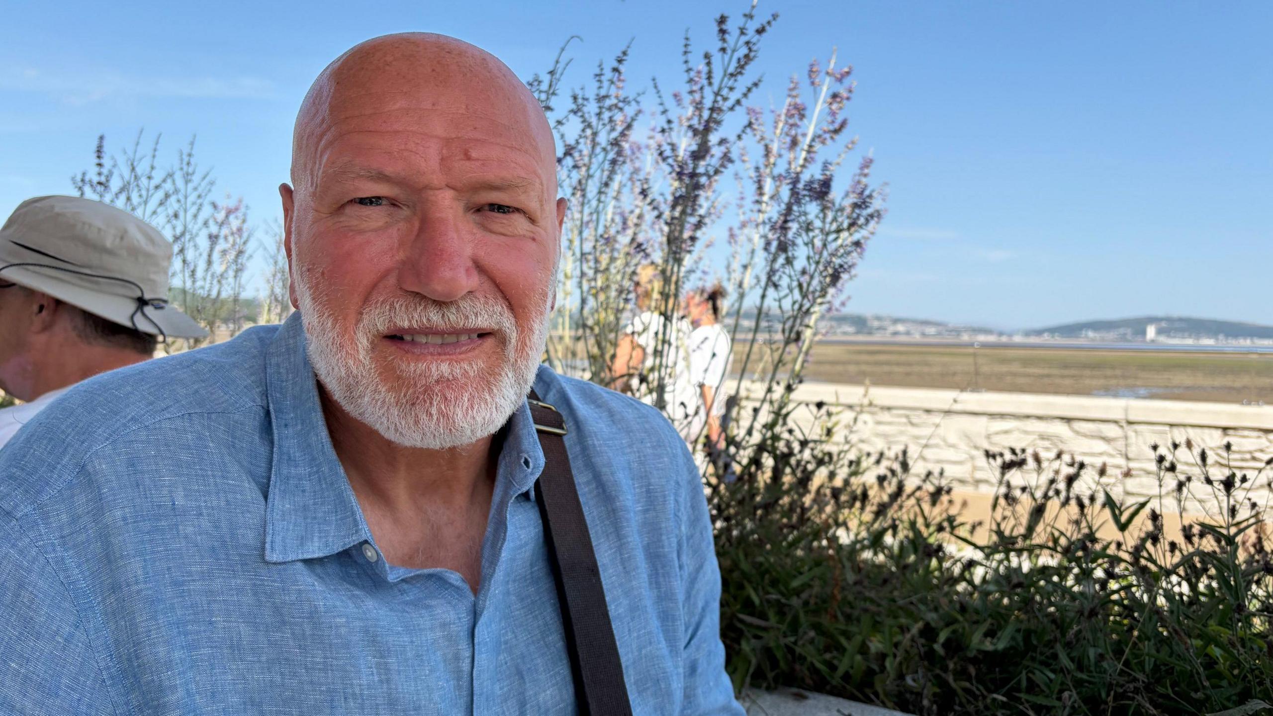 A man in a blue shirt with a white beard sat on Mumbles seafront.