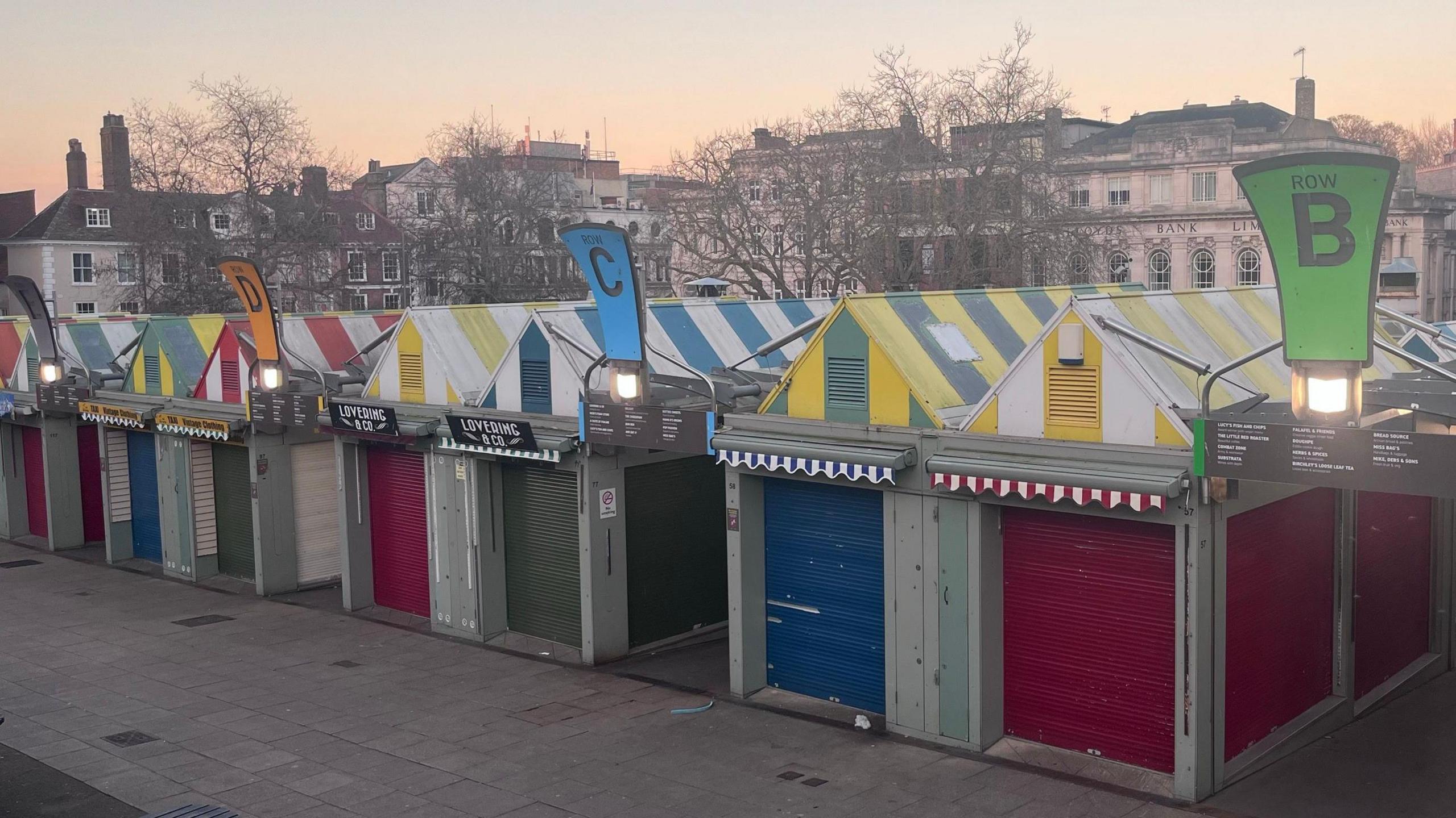 Norwich markets. Rows of market stalls with coloured metal shutters and striped colourful roofs. 