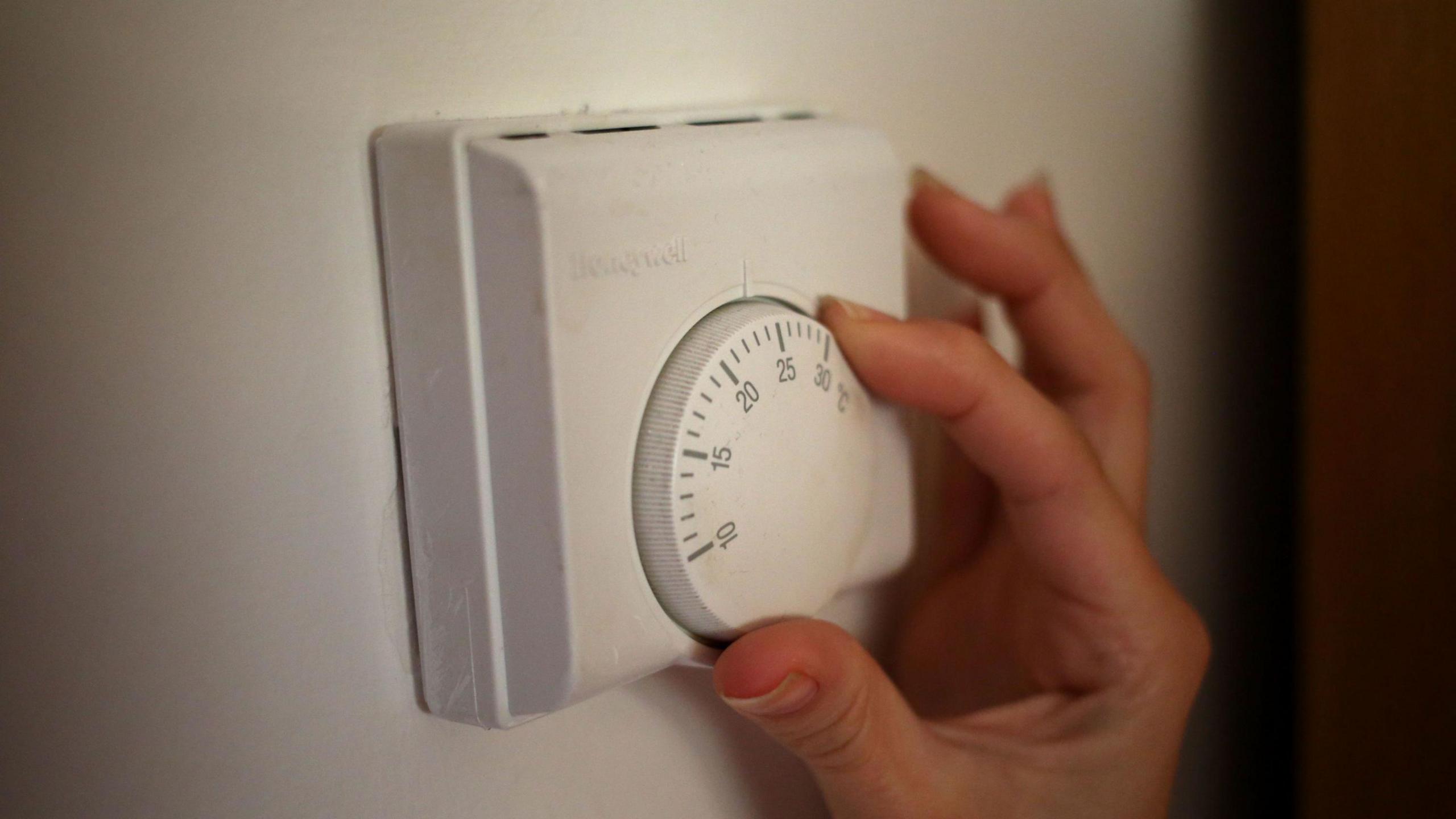 A person using a central heating thermostat. The thermostat is white and has a round dial to select the correct heat.