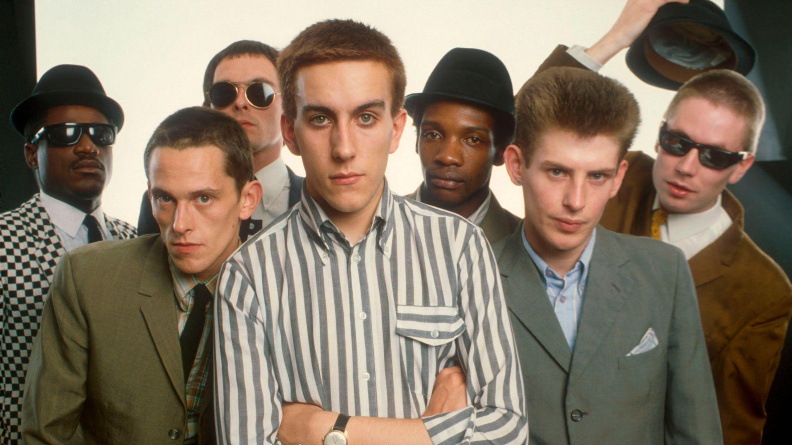 The seven members of the Specials - wearing suits and looking into the camera. Three of the group are wearing hats, with one band member on the right lifting his off.