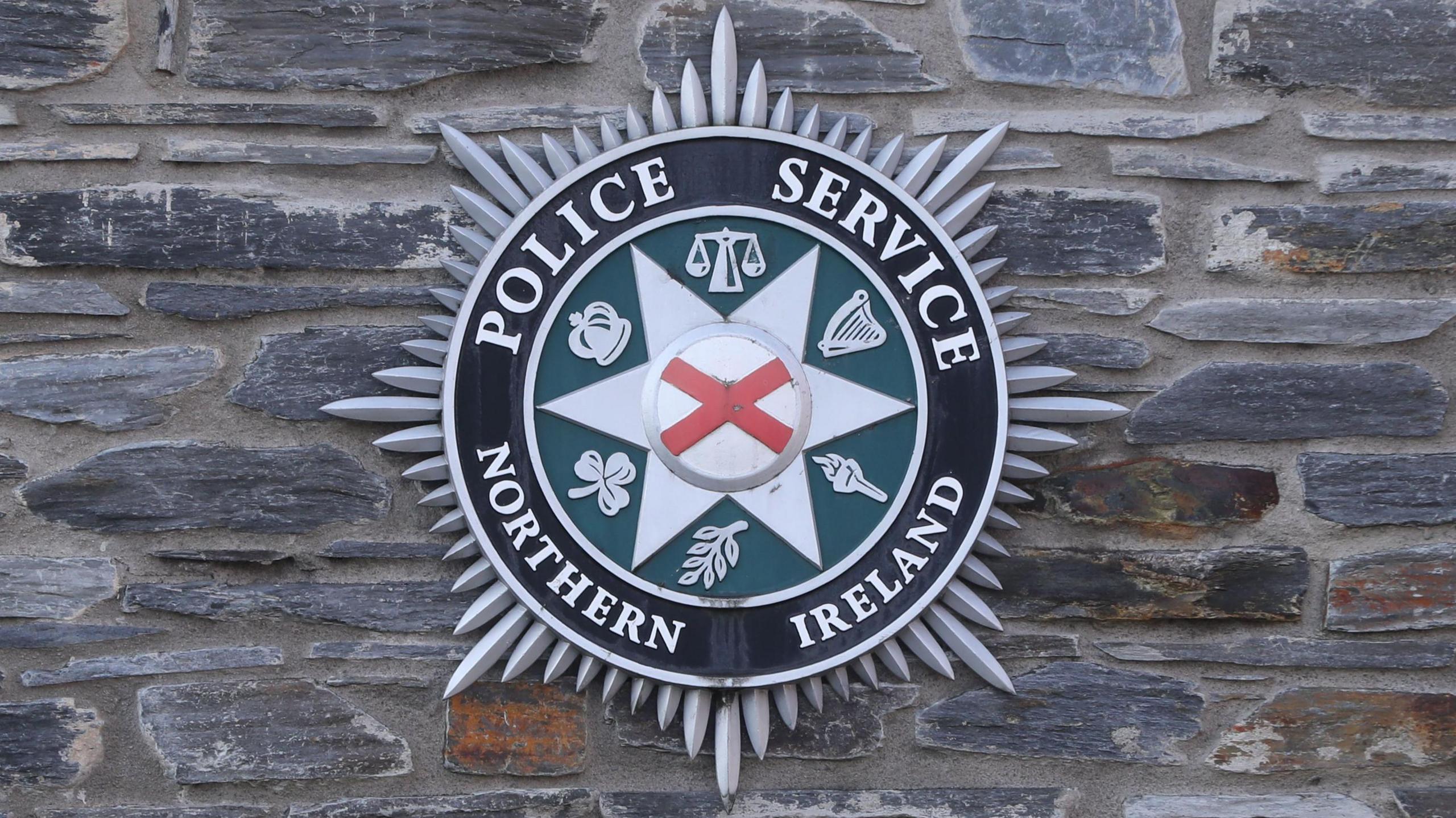 A Police Service of Northern Ireland (PSNI) logo badge on a grey stone wall.