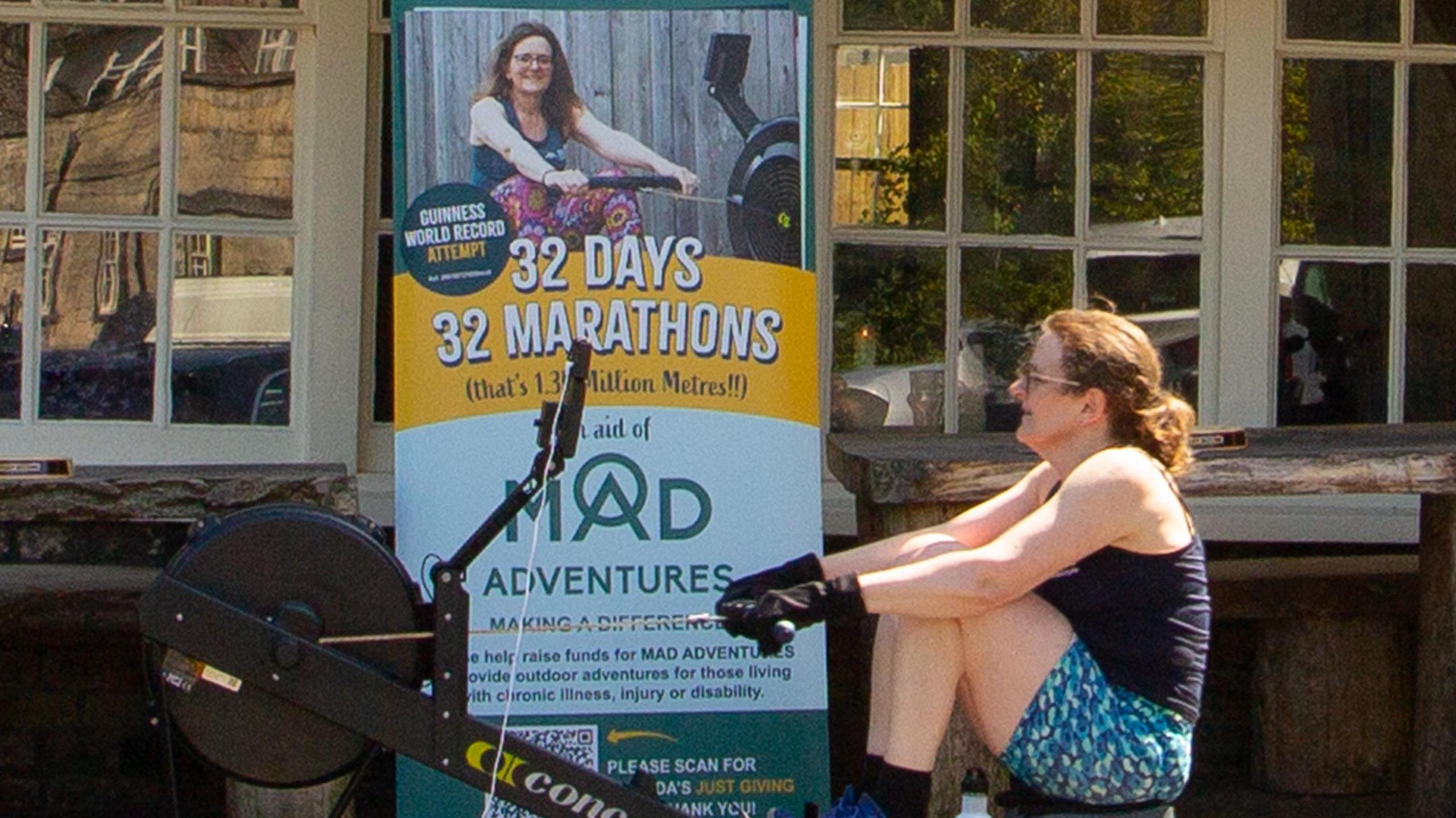 Woman on rowing machine in front of her charity board