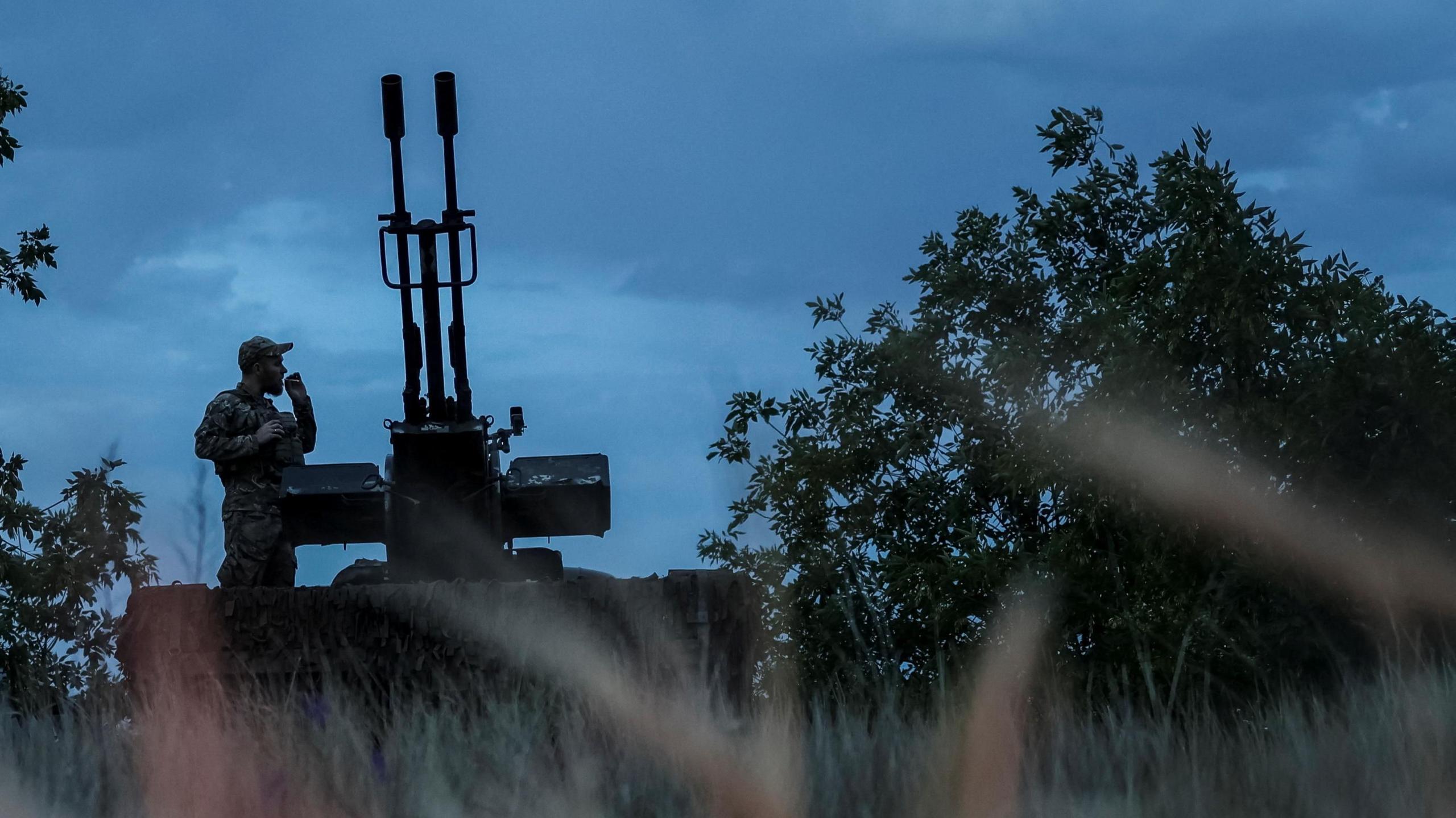 A man smokes a cigarette standing next to an anti-aircraft gun in the Kherson region of Ukraine.