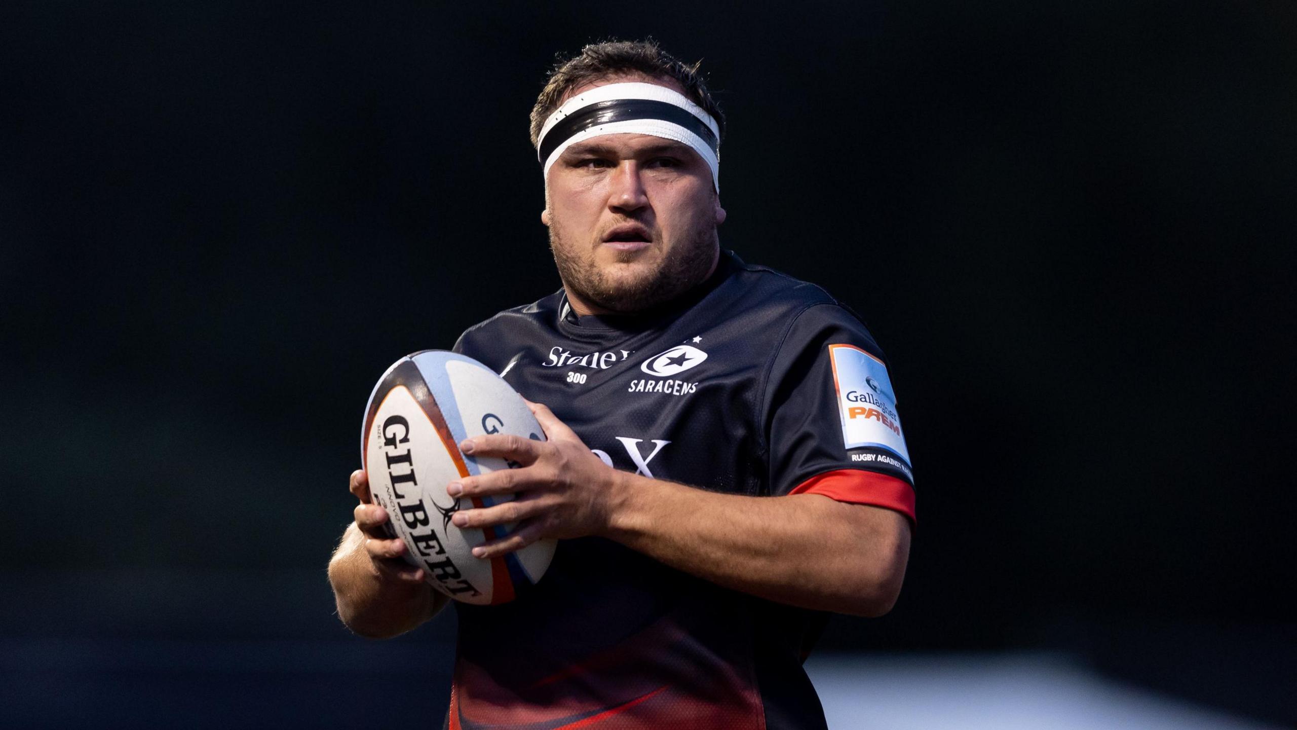 Jamie George holding a ball between his two hands close to his body while standing on the pitch during a match for Saracens last season