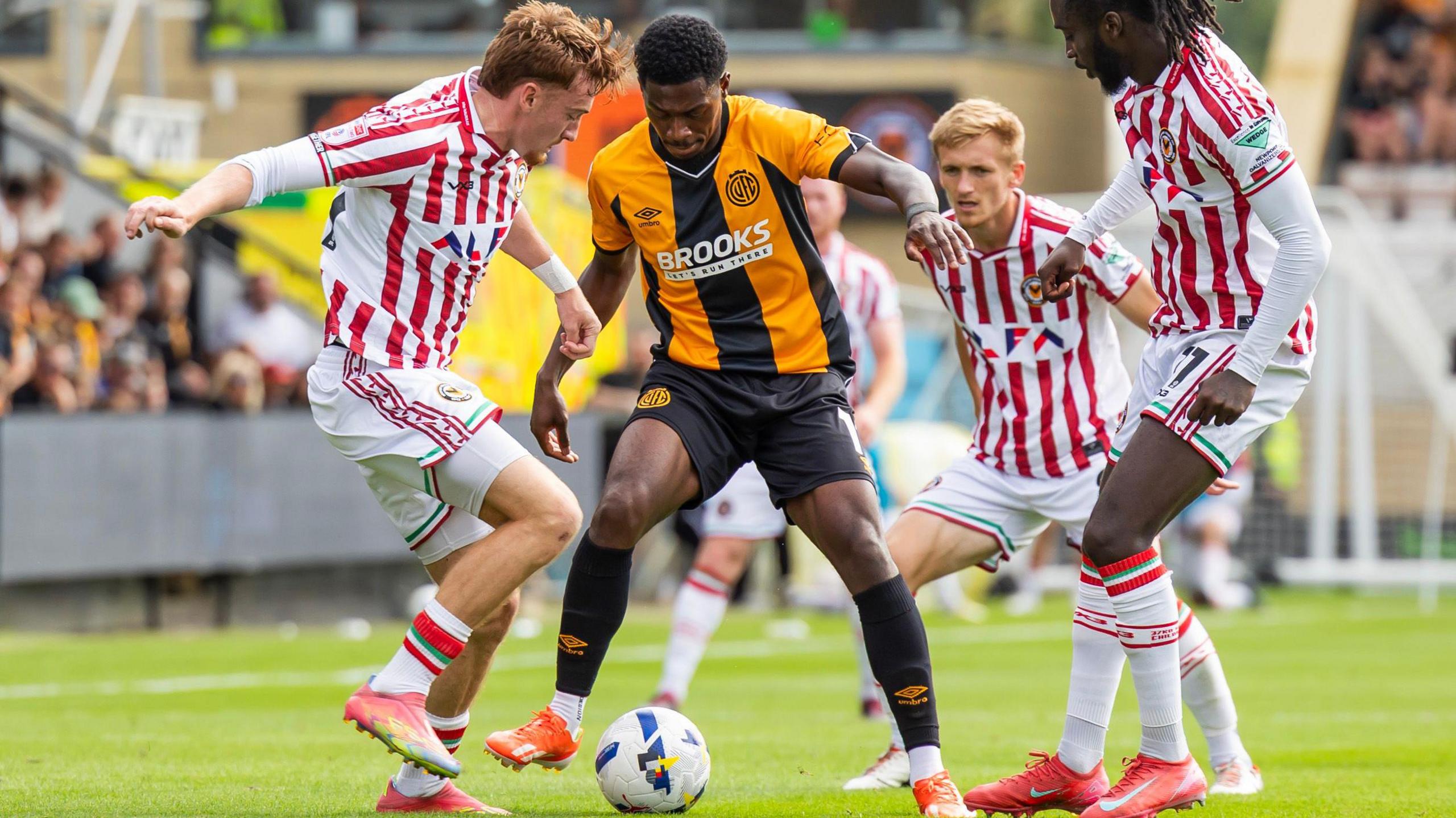 Newport County players swarm around Sulley Kaikai of Cambridge