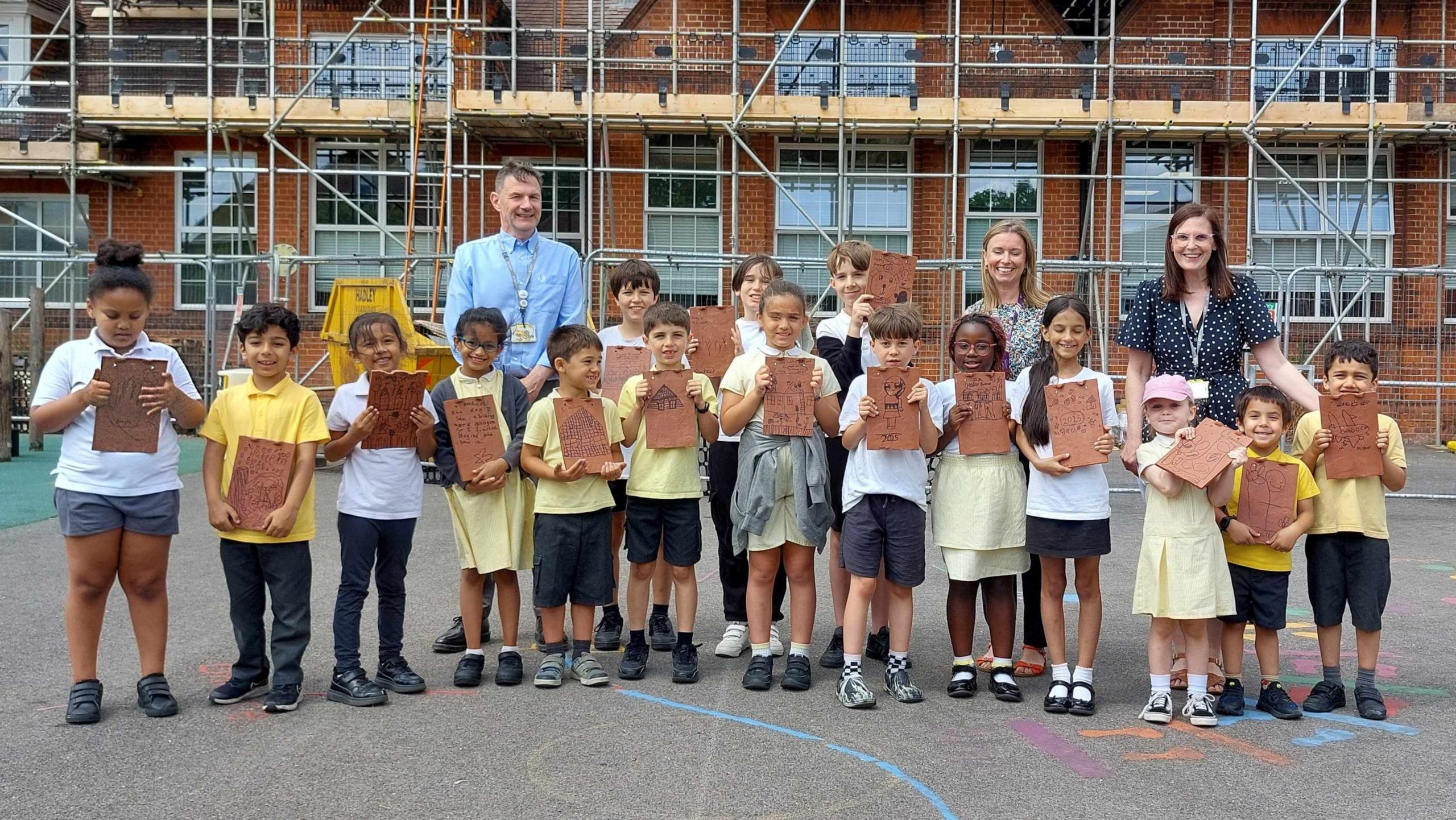 Teachers and children looking at the camera holding their decorated tiles.