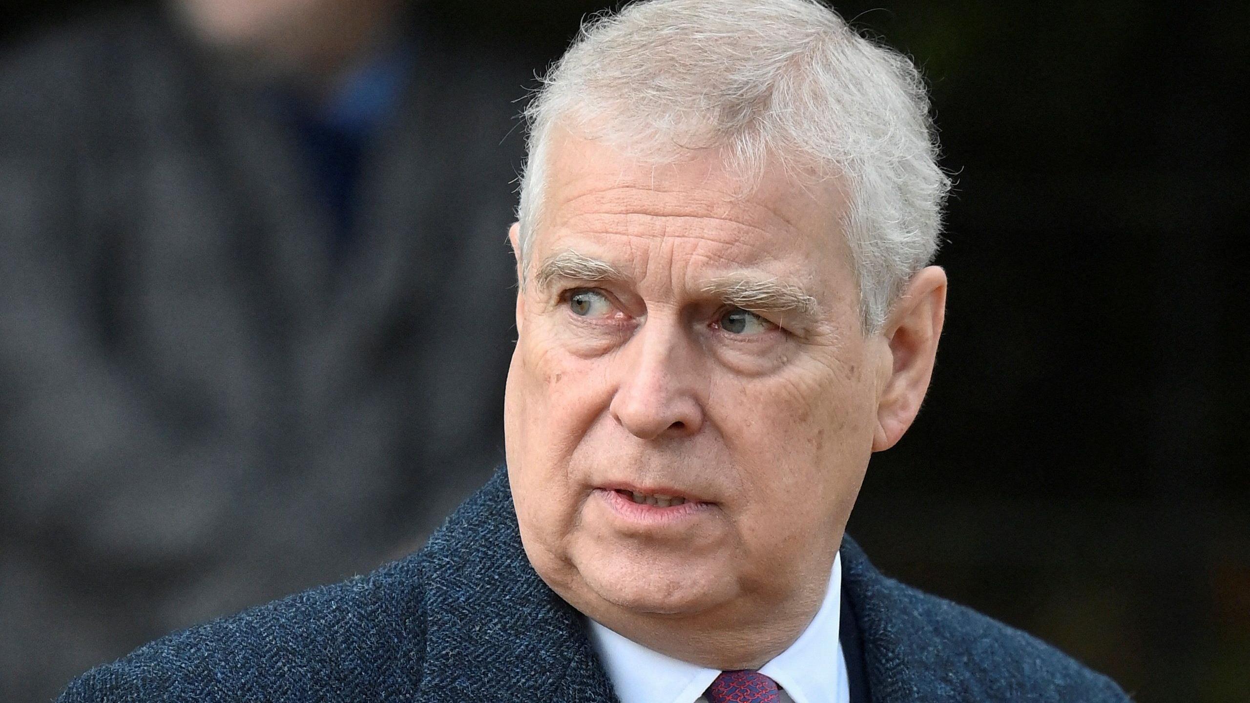 Prince Andrew in a blue jacket, white shirt and red tie. He has grey hair.