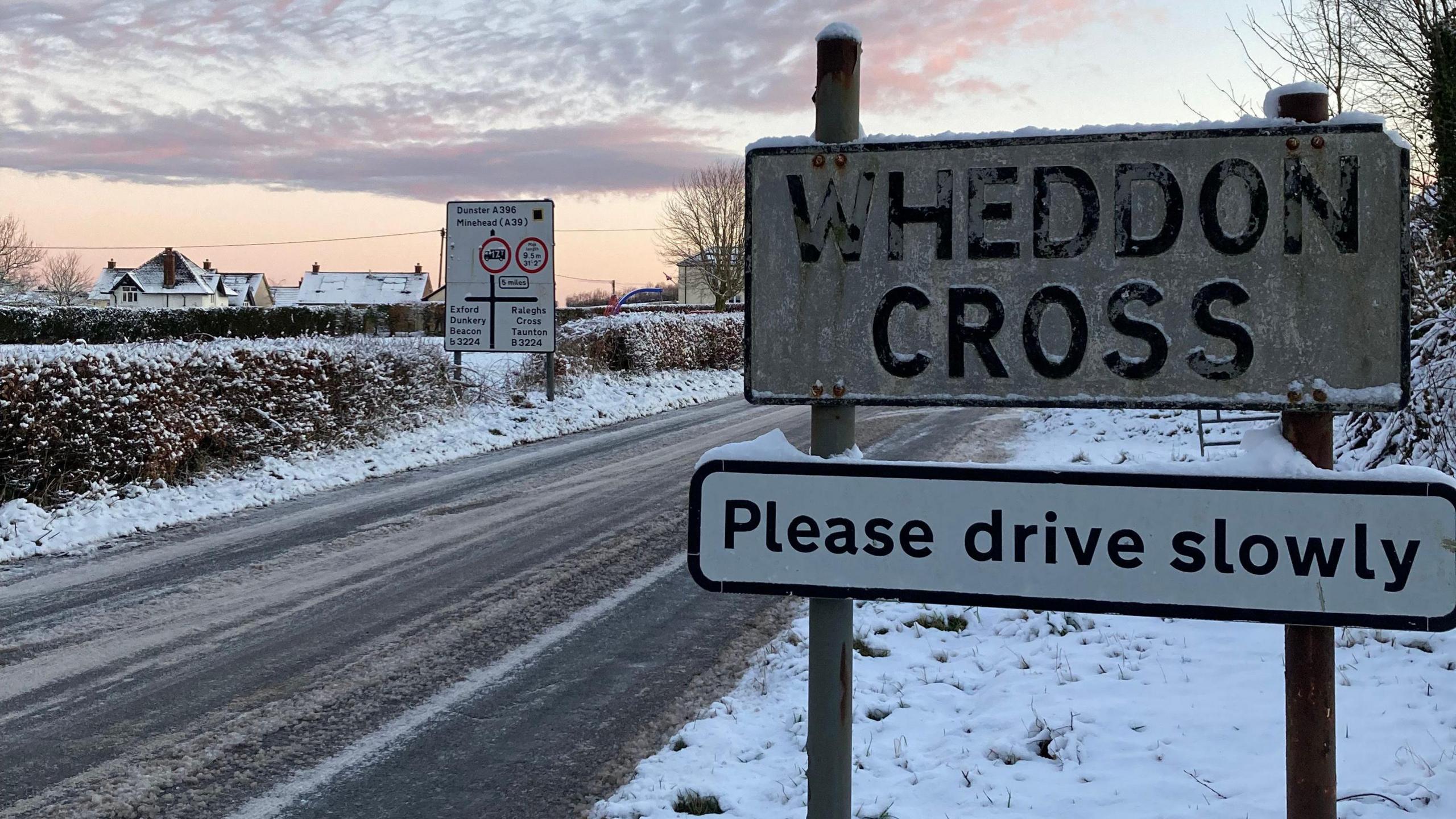 An icy road with a sign that says 'Wheddon Corss please drive slowly'