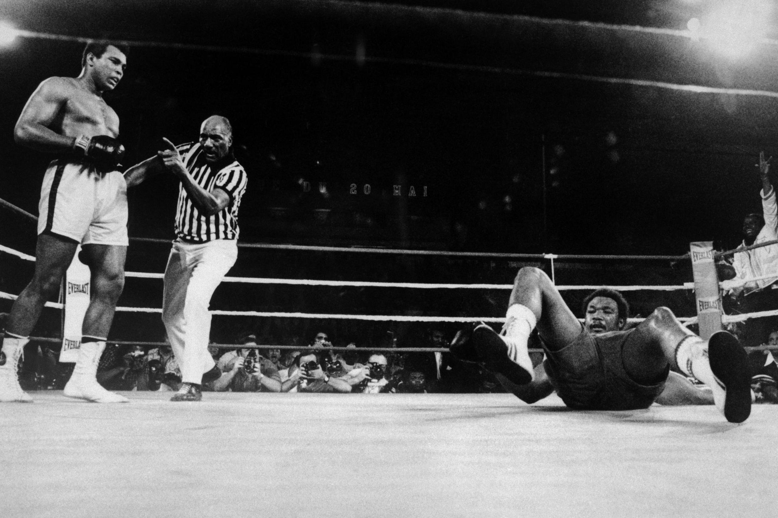 Foreman on the ground with Ali and the referee standing to his left