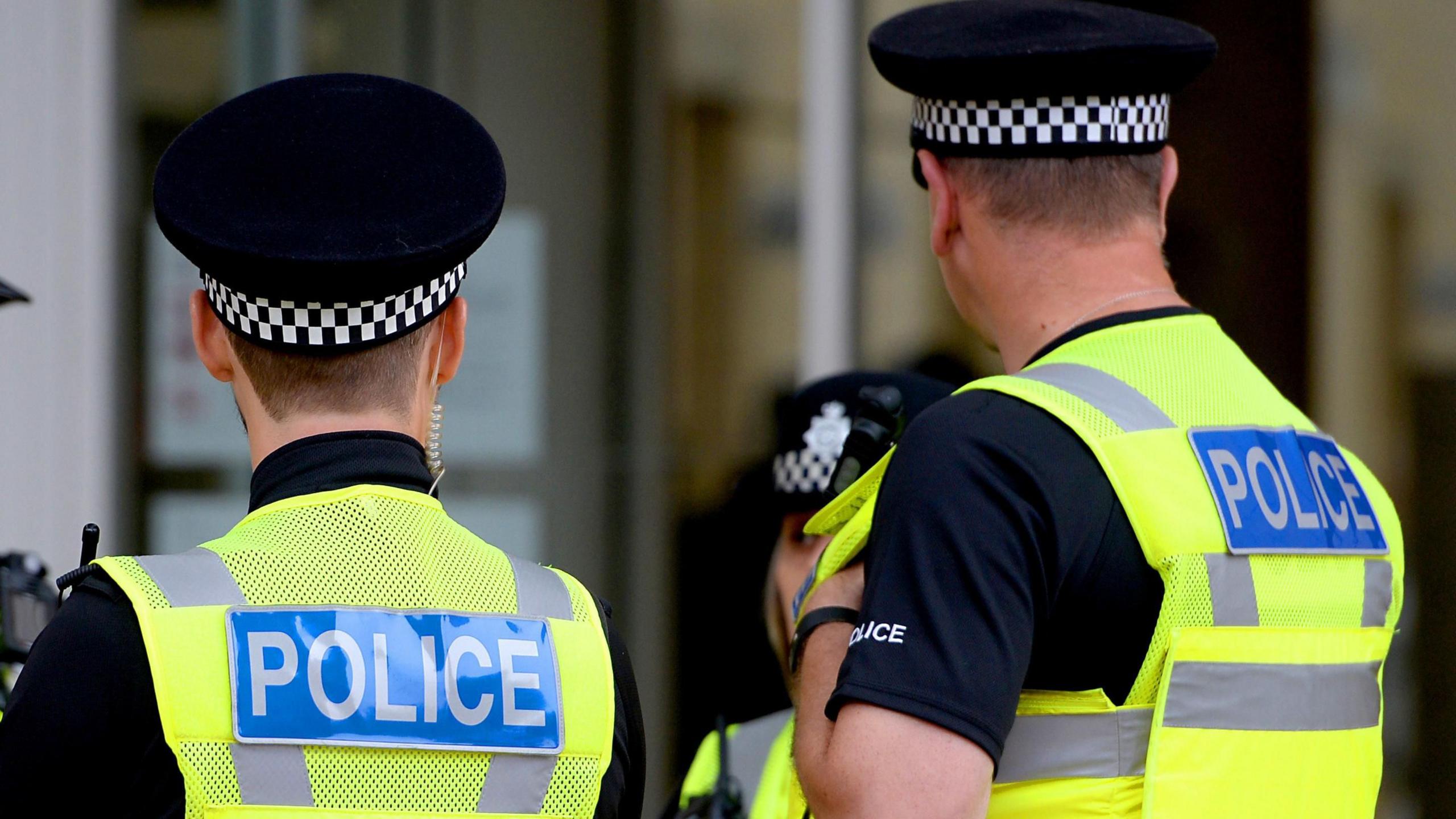 The back of two police officers wearing fluorescent stab vests