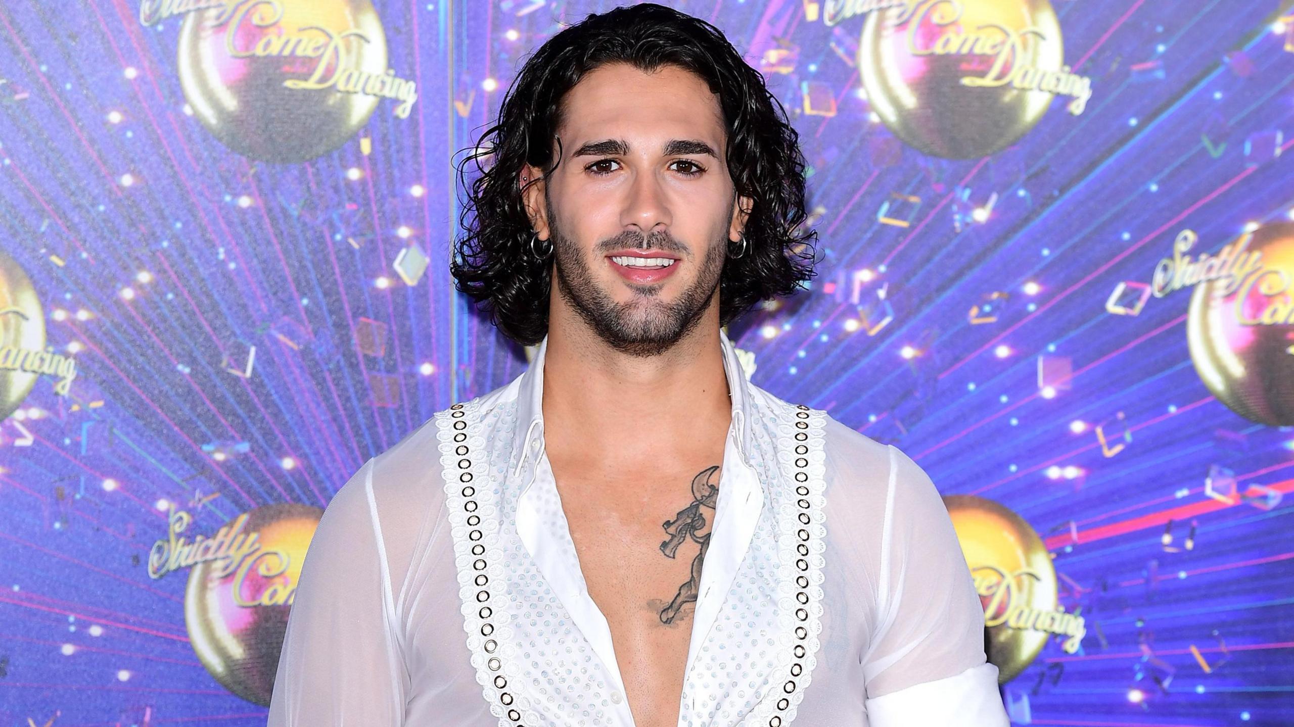 Graziano Di Prima stands in a white shirt with Strictly Come Dancing banner in the background