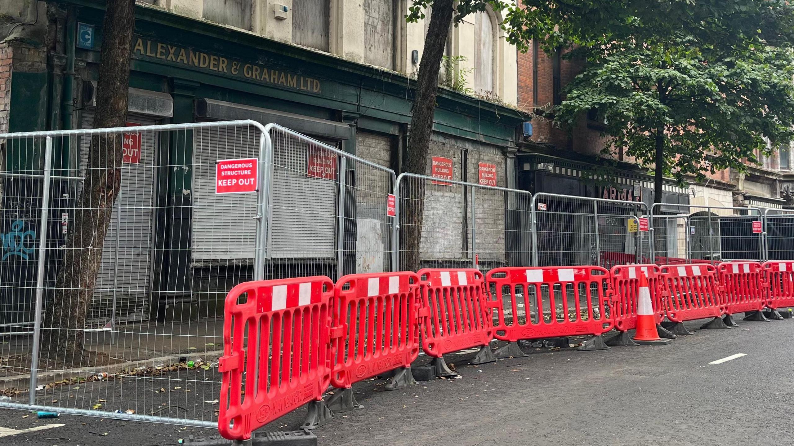 A red safety barrier set up along a road outside a derelict building. 