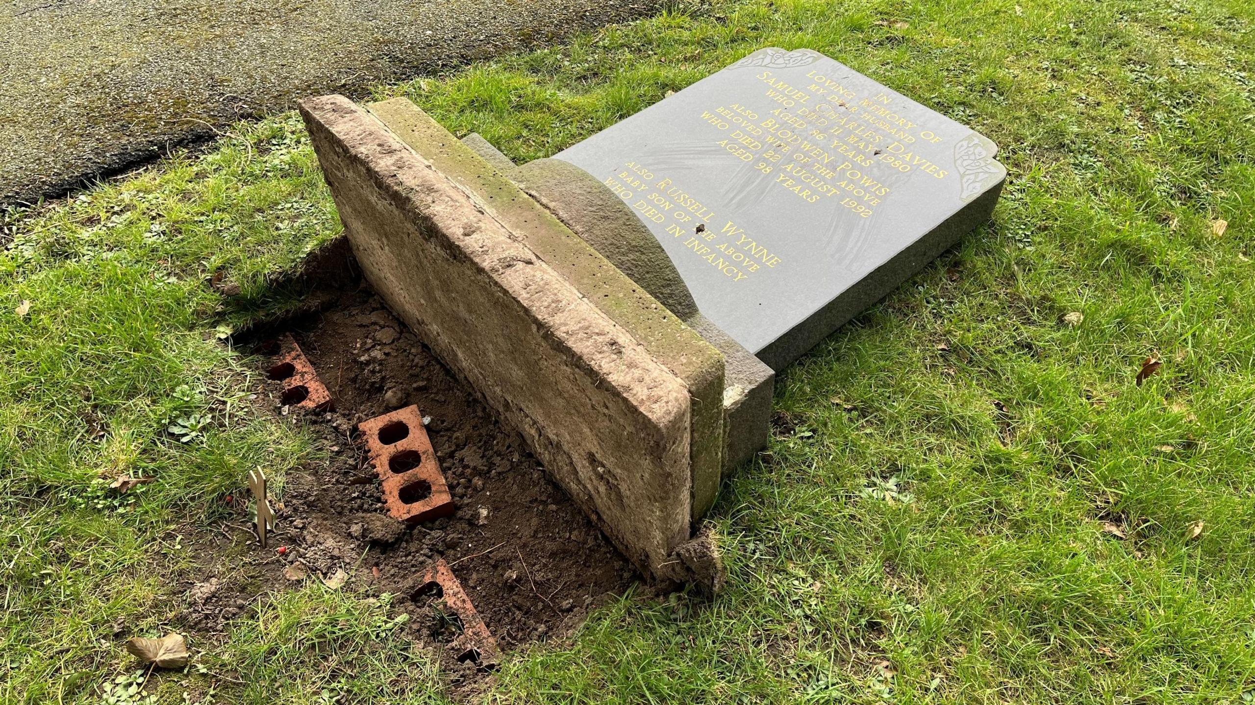 Picture shows a grave headstone uprooted from the ground. 