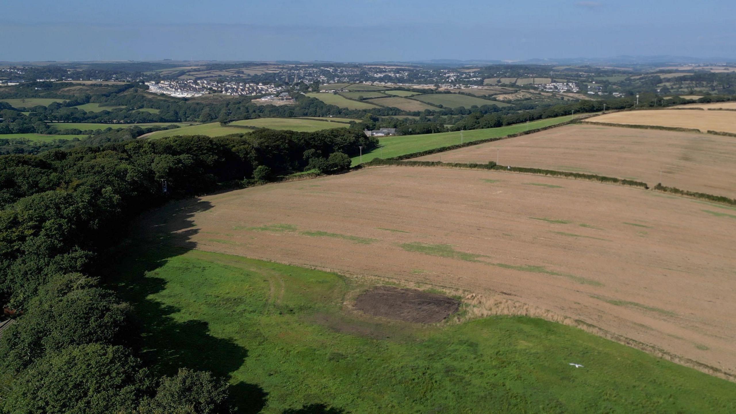 An aerial view over a number of fields and wooded areas with a view of Truro on the horizon.
