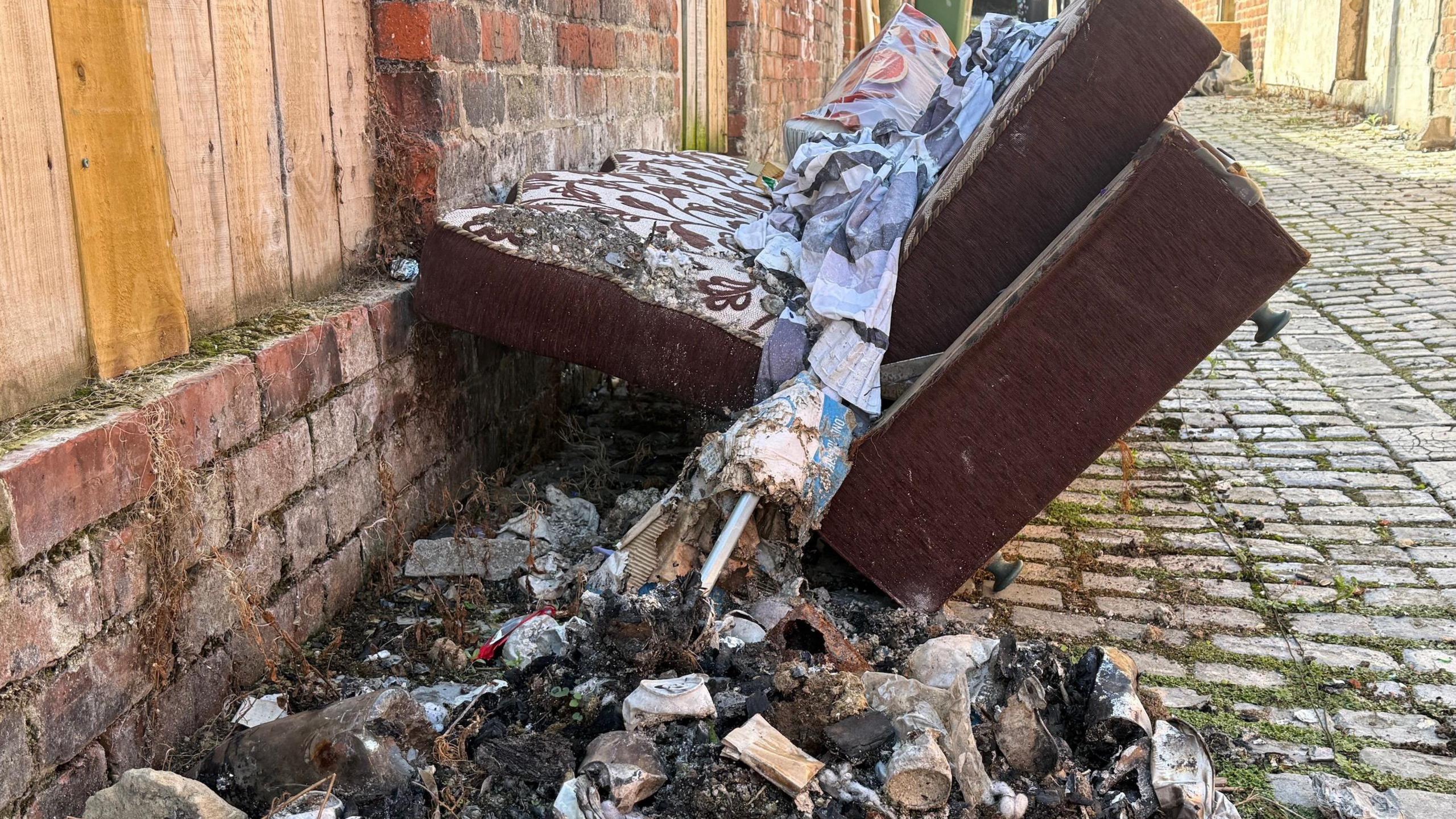 An old sofa dumped in a cobbled alleyway alongside burnt rubbish