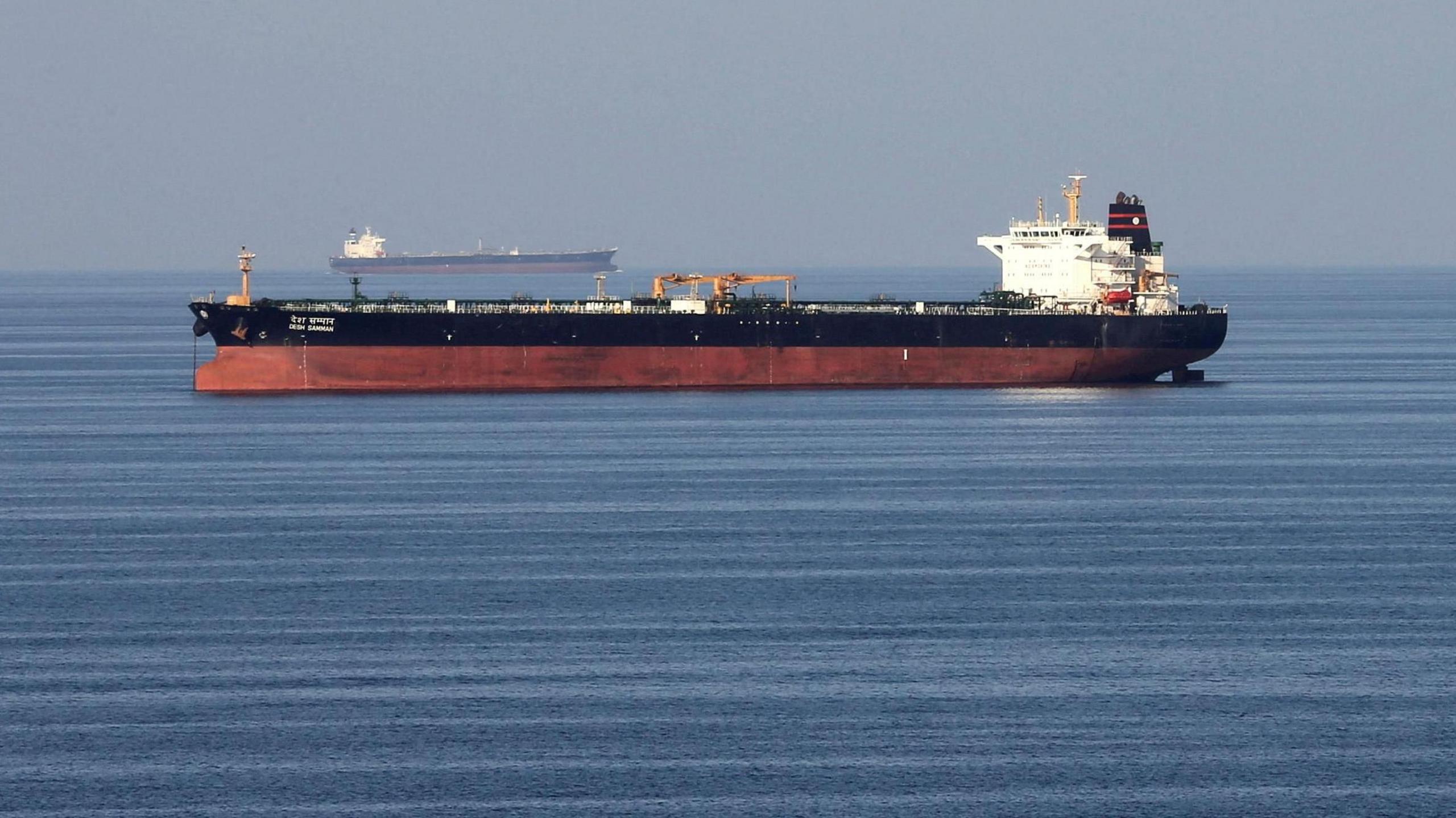 Oil tankers pass through the Strait of Hormuz. Both ships have a red lower section and dark upper section with a white tower. They are heading in opposite directions