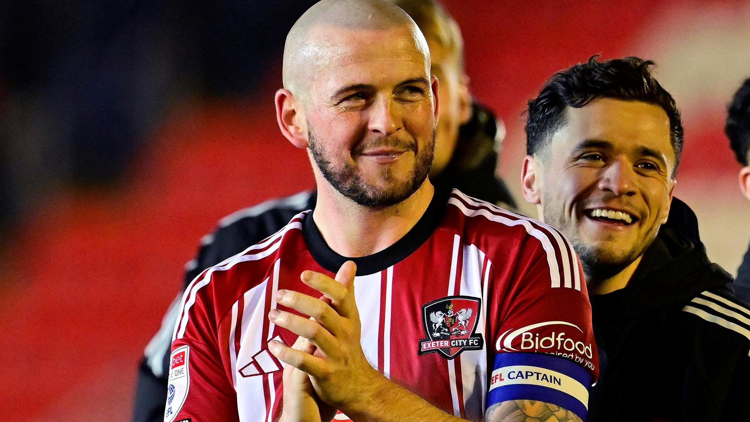 Pierce Sweeney, wearing Exeter City's red and white kit, applauds supporters