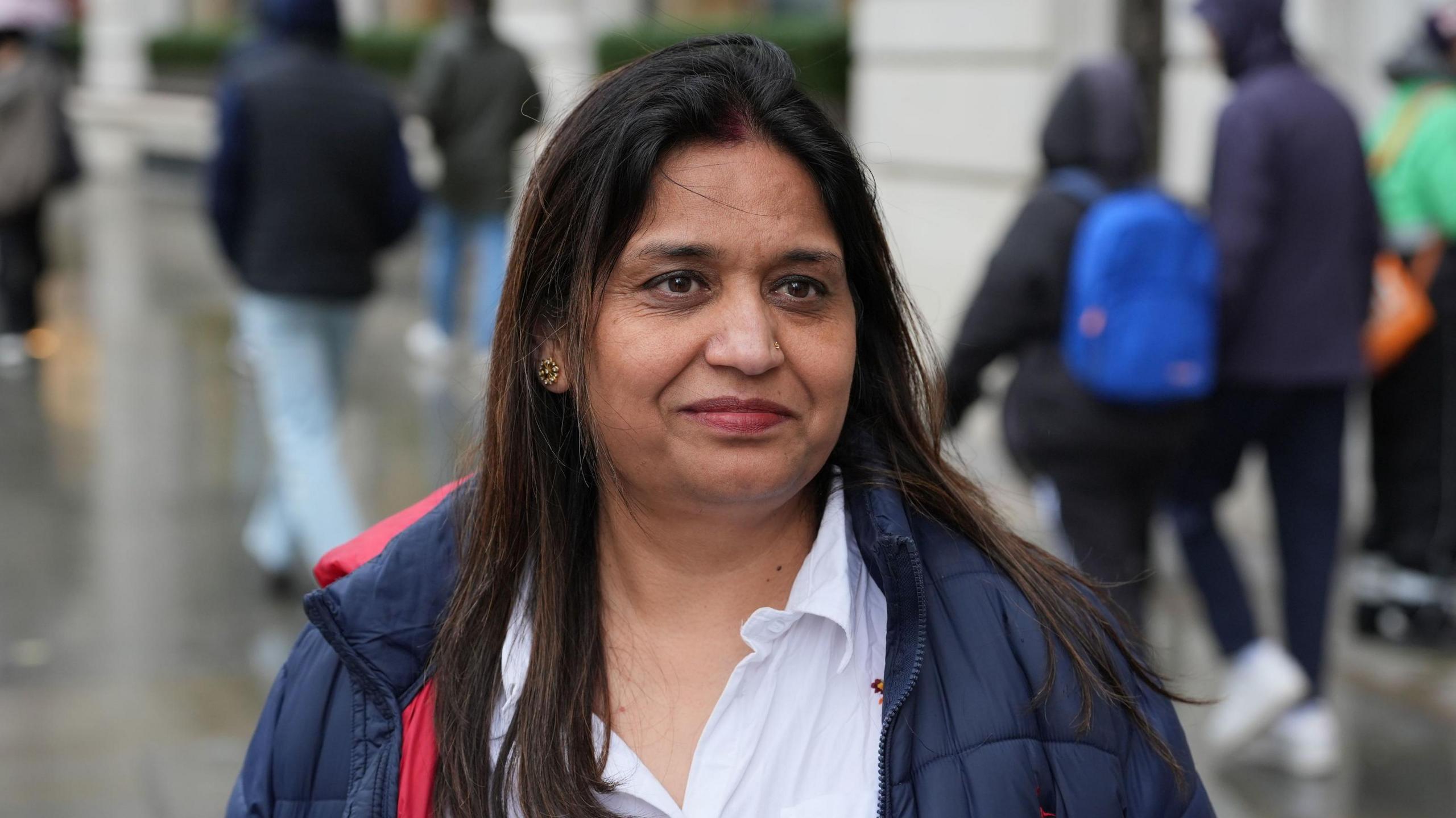 Seema Misra smiling with people walking in the street behind her