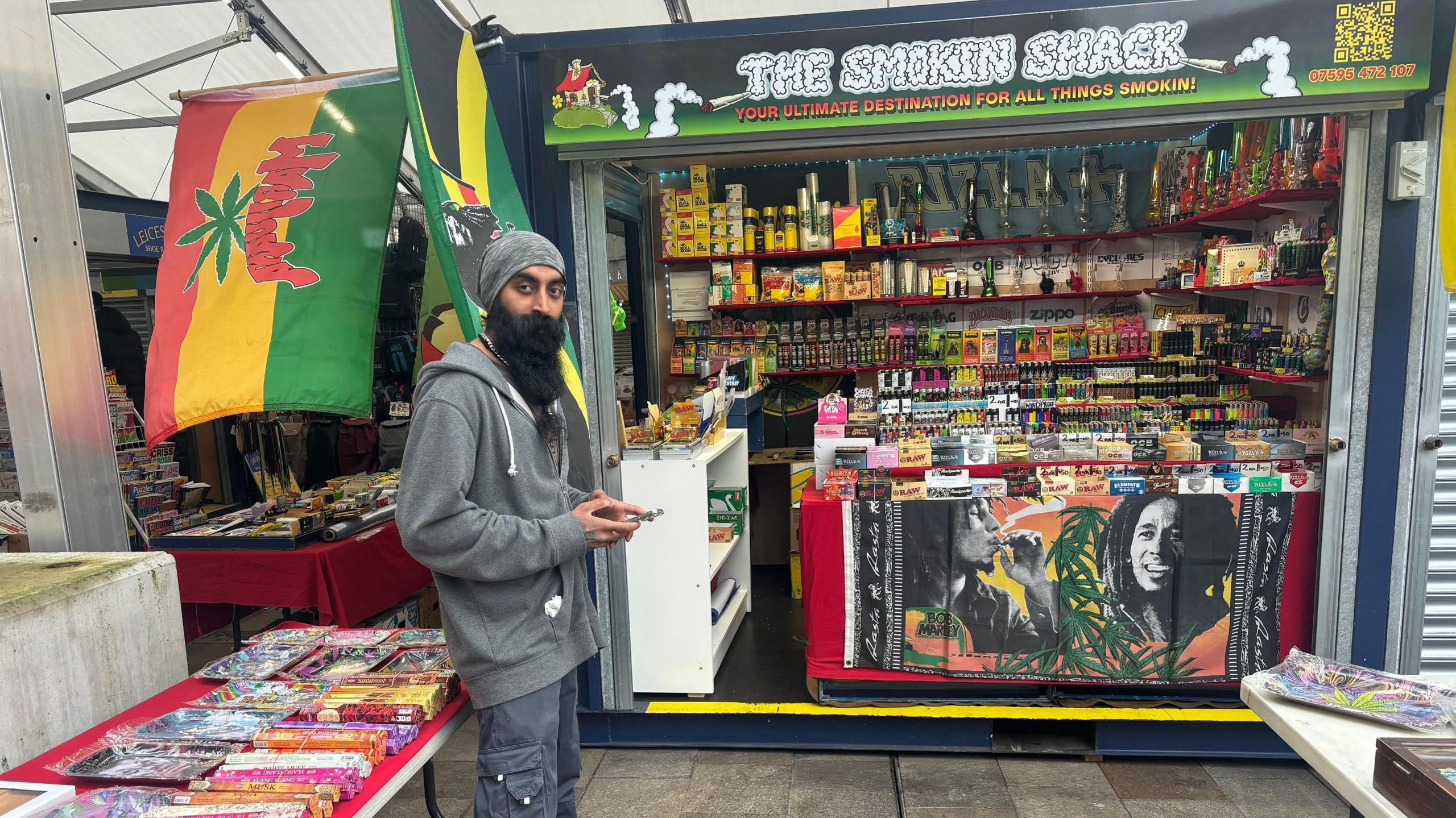 A trader standing by his stall with smoking paraphernalia, incense sticks and flags on display.