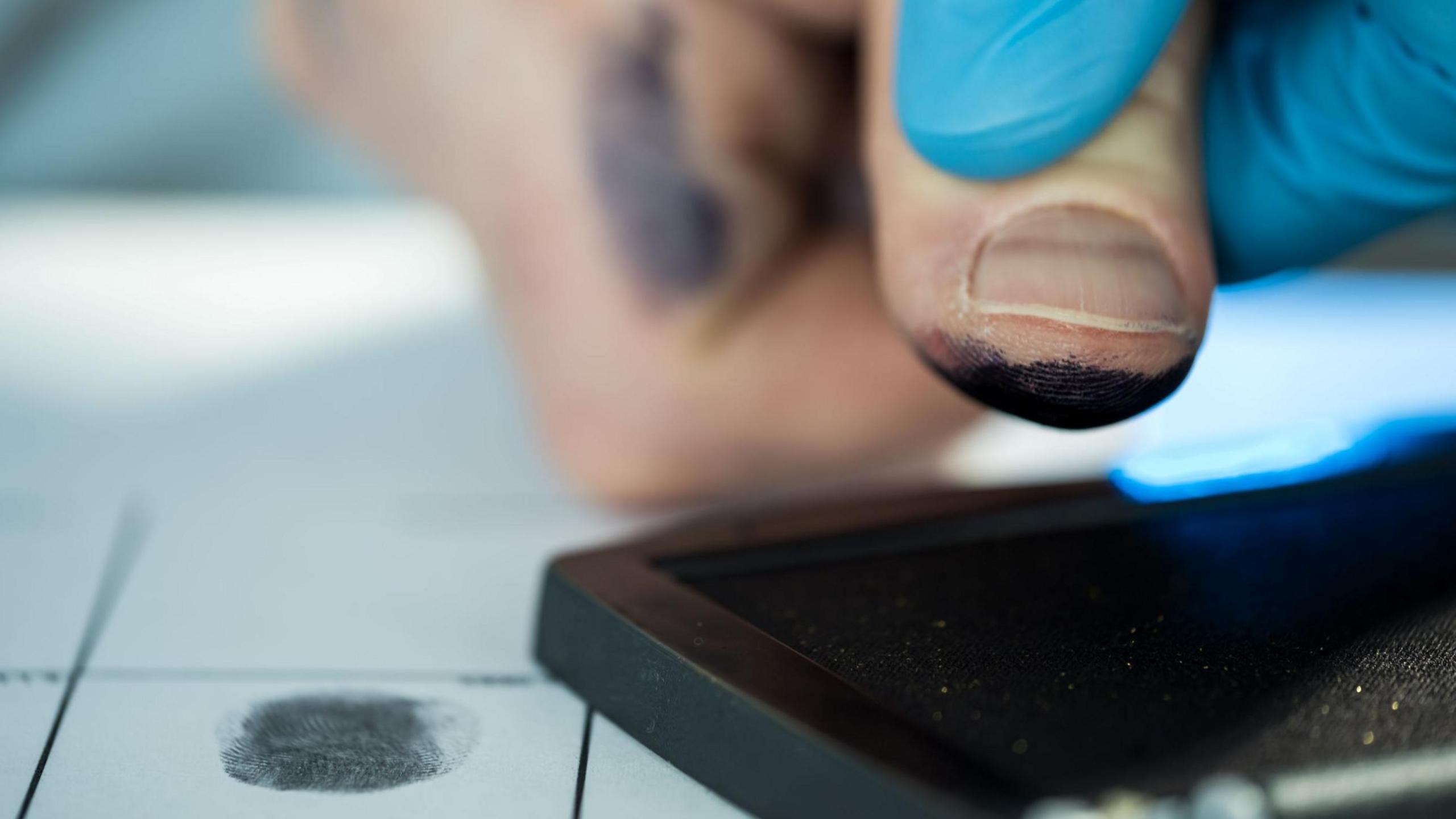 A person has their prints taken by a person wearing protective blue gloves.