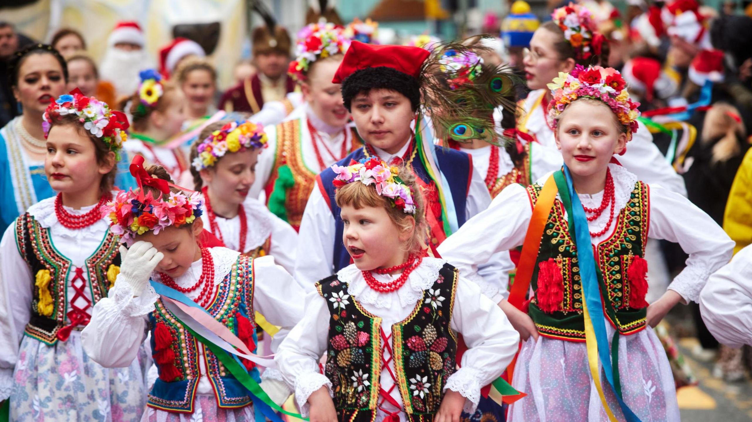 Child performers decked out in mainly floral headdresses and colourful embroidered waistcoats over white tunics