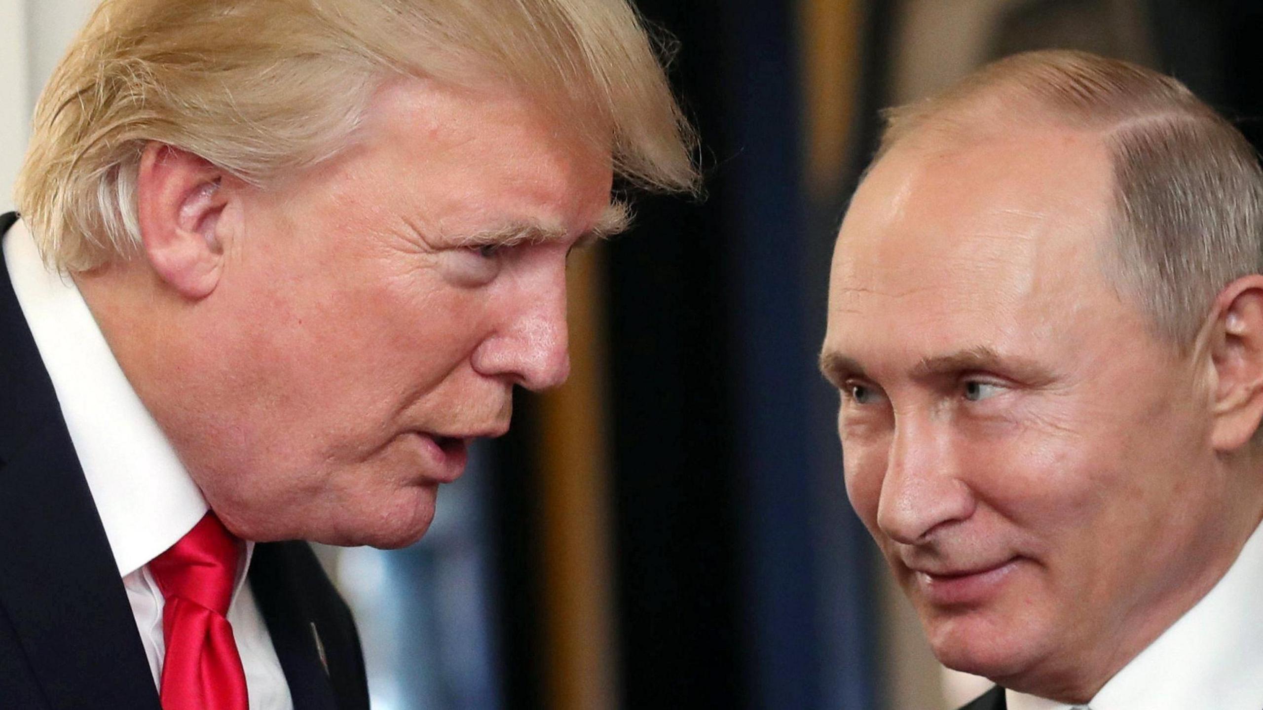 Donald Trump, seen close up in profile from the right, wears a dark suit and white shirt with red tie. He is talking to Vladimir Putin, who is smiling enigmatically.