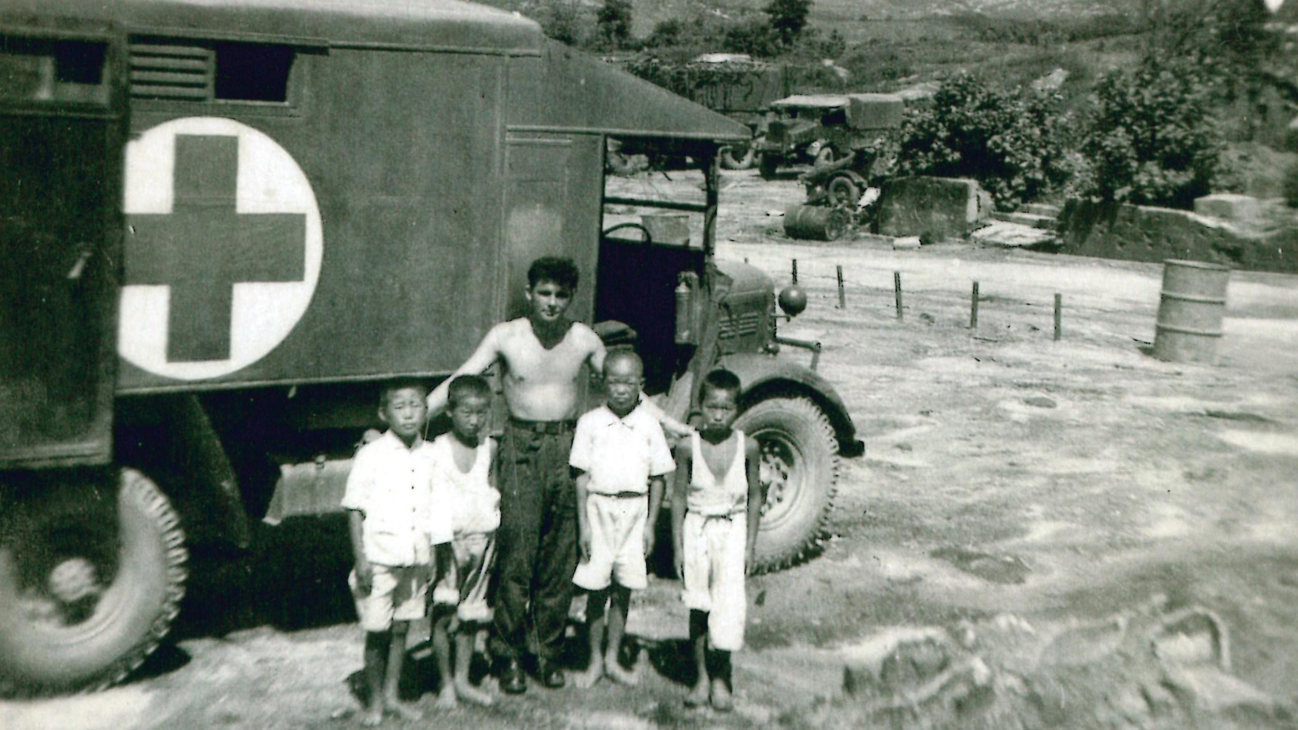 Albert Morrow centre, with four children wearing light coloured clothing, in front of an ambulance van