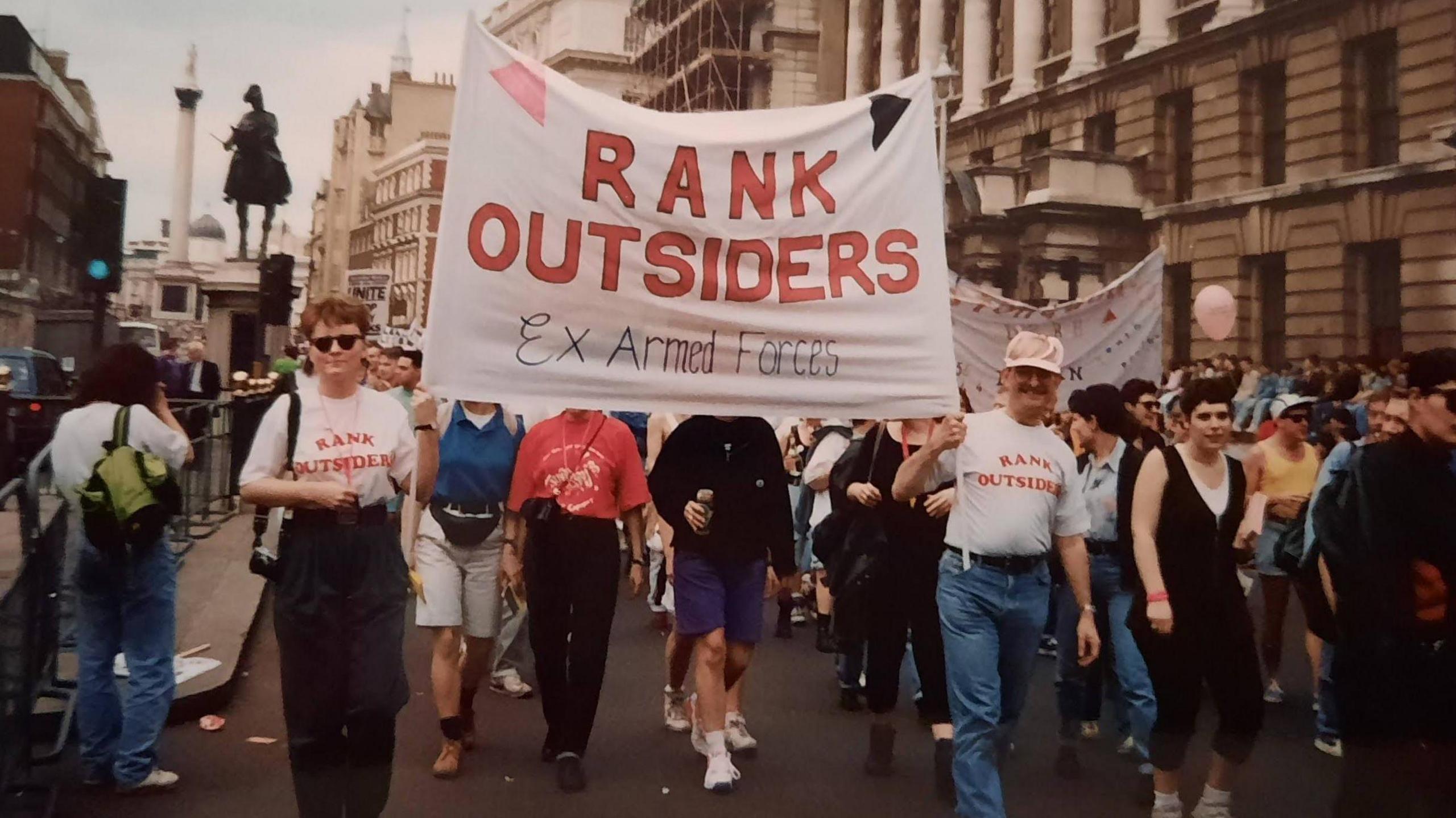 An archive photo of a protest by the Rank Outsiders, which is written on a banner held aloft at the front of a march in central London. Trafalgar Square's Nelson's Column monument can be seen in the background behind them.
