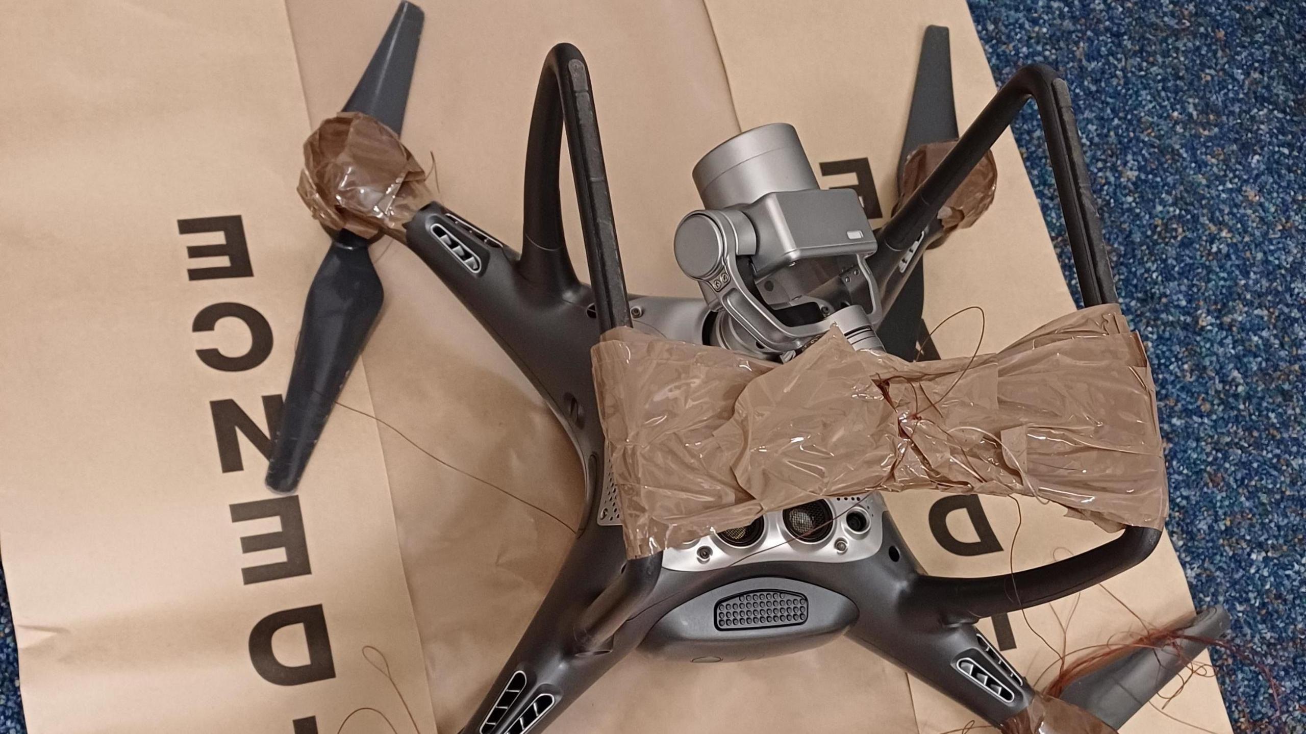 A black and silver unmanned drone, which has four arms fitted with propellers, placed on a brown bag marked 'evidence'