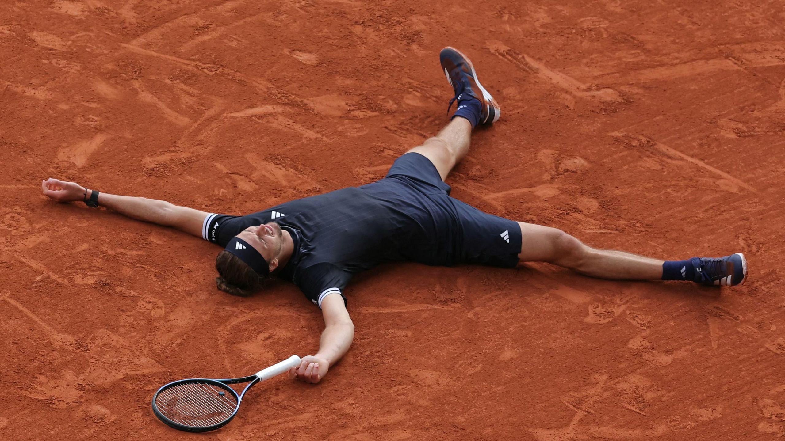 Alexander Zverev lies on the Roland Garros clay after winning the men's title