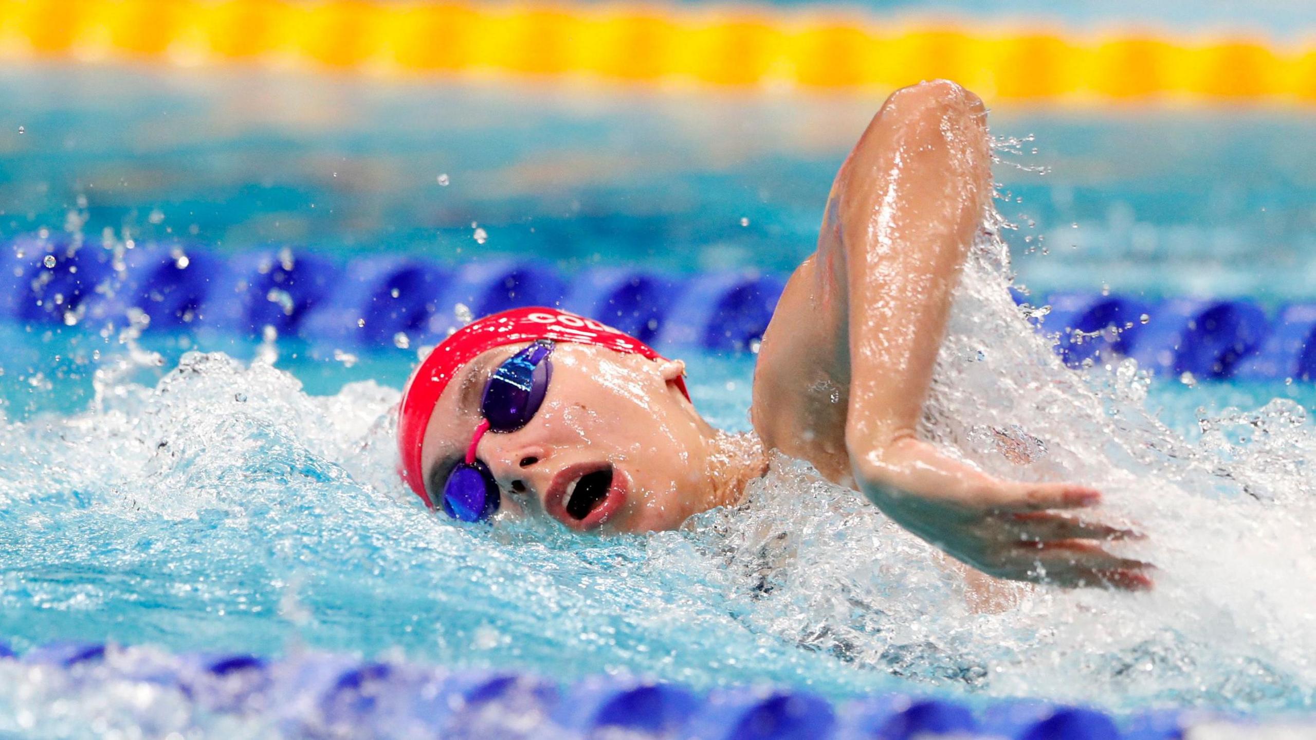 Swimmer Freya Colbert wears a red swimming cap and goggles as she competes in the pool