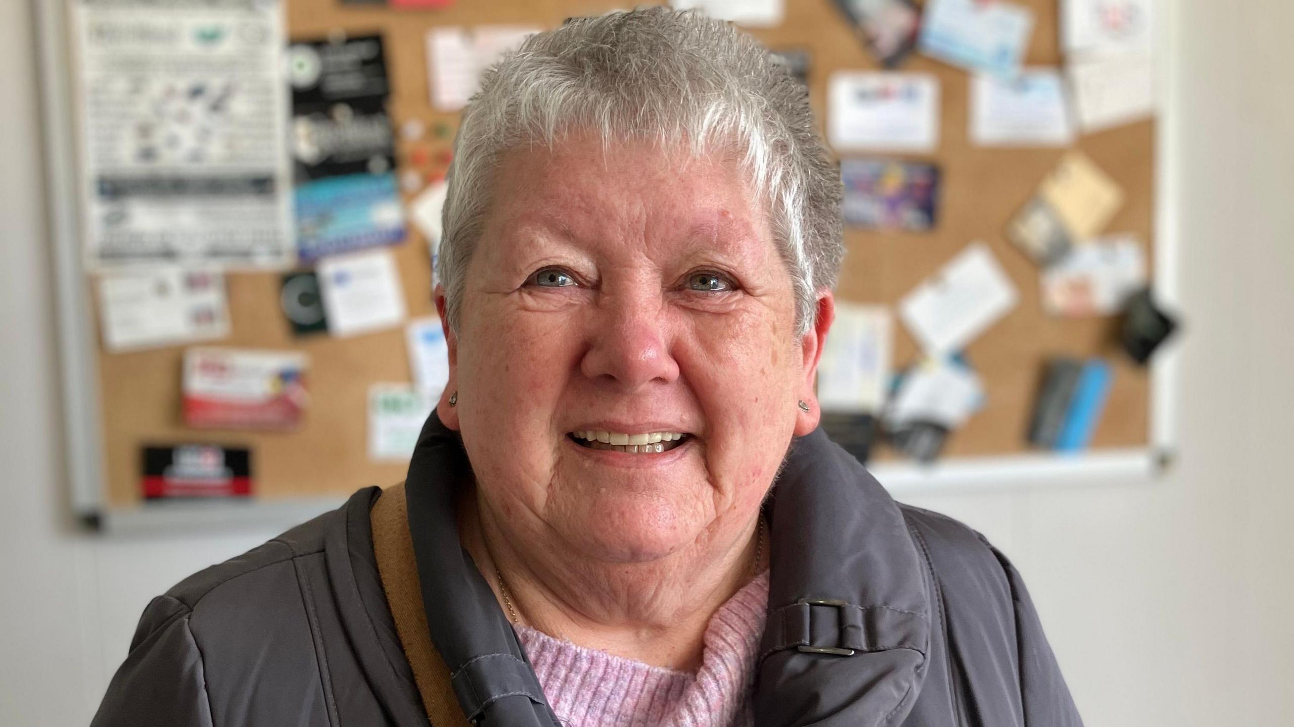 Linda Aldis, who has short grey hair and blue eyes. She is smiling towards the camera.