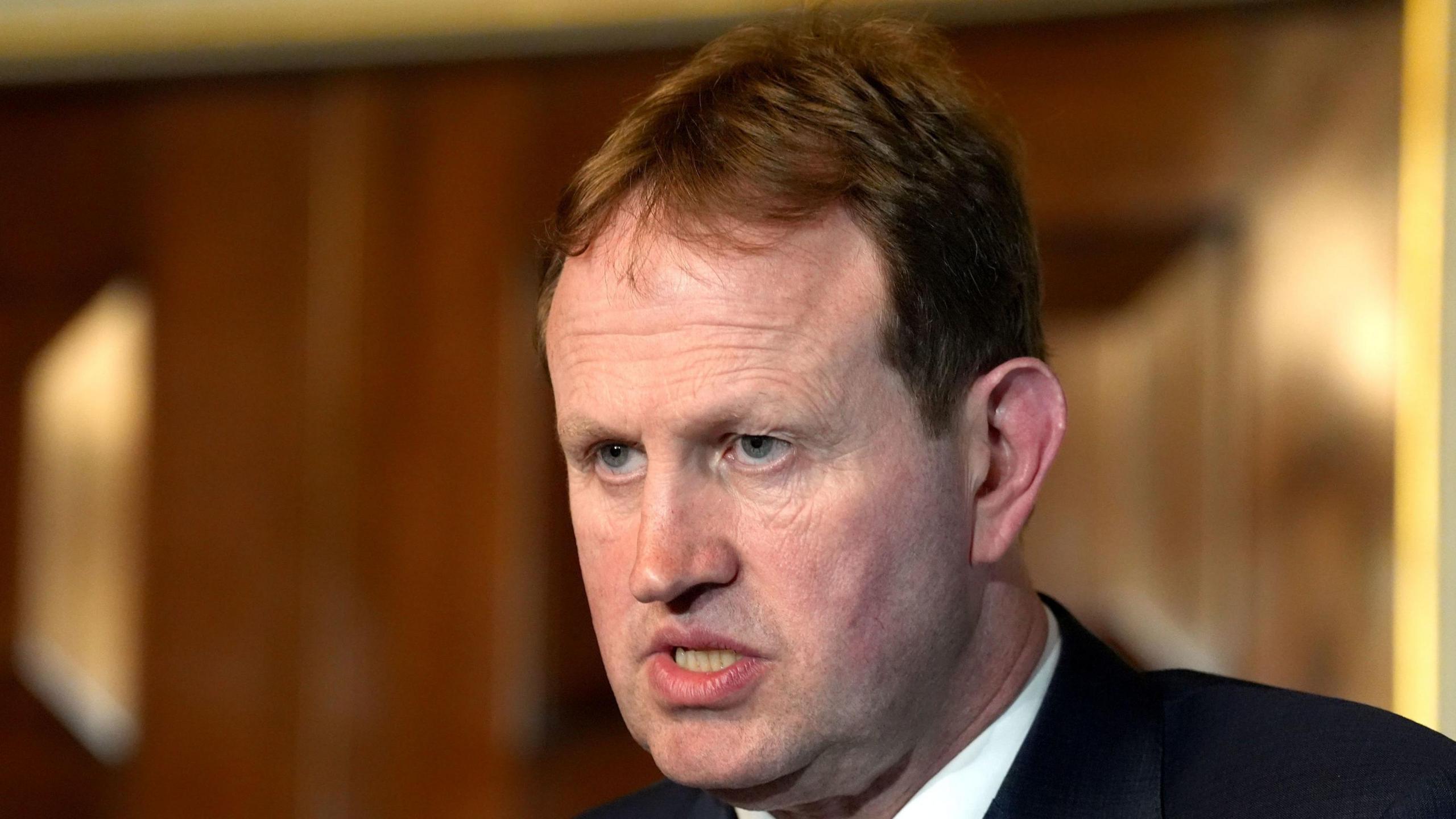 Jim O'Callaghan has short ginger hair and is wearing a black suit with a white shirt. He is speaking in a wooden walled room.