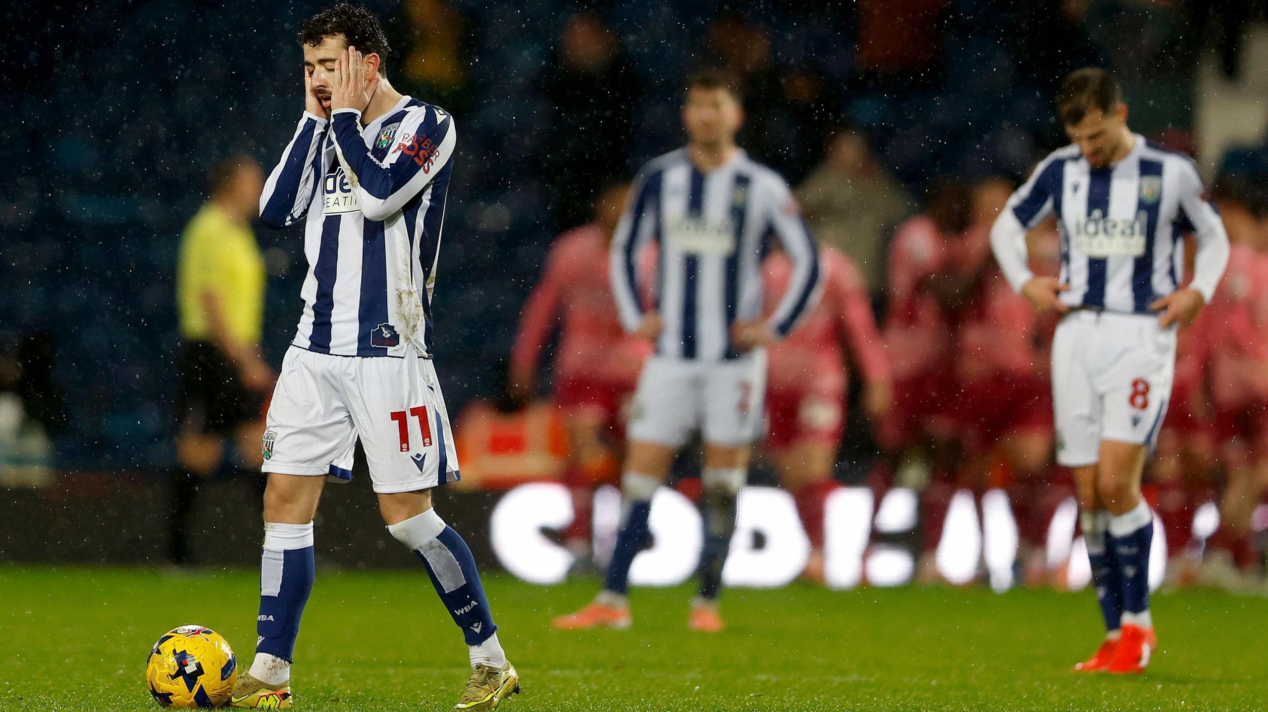 West Brom player Mikey Johnston holds his head in his hands during his side's 5-0 defeat to Norwich City as his team-mates look frustrated in the background. 