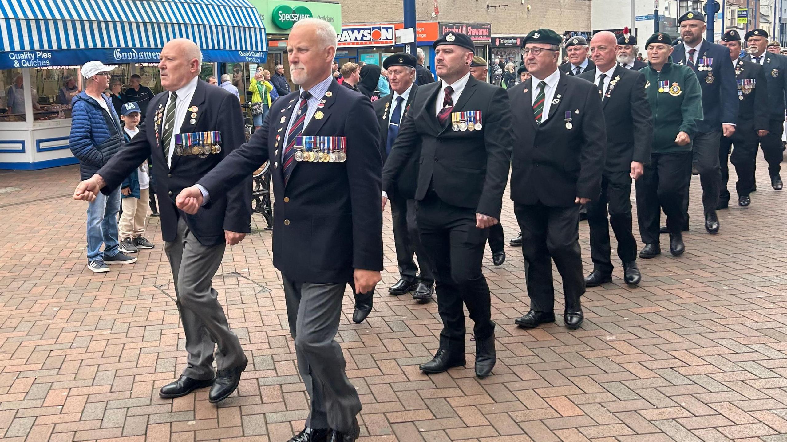 A street parade of smartly dressed military personnel wearing their medals and marching two by two