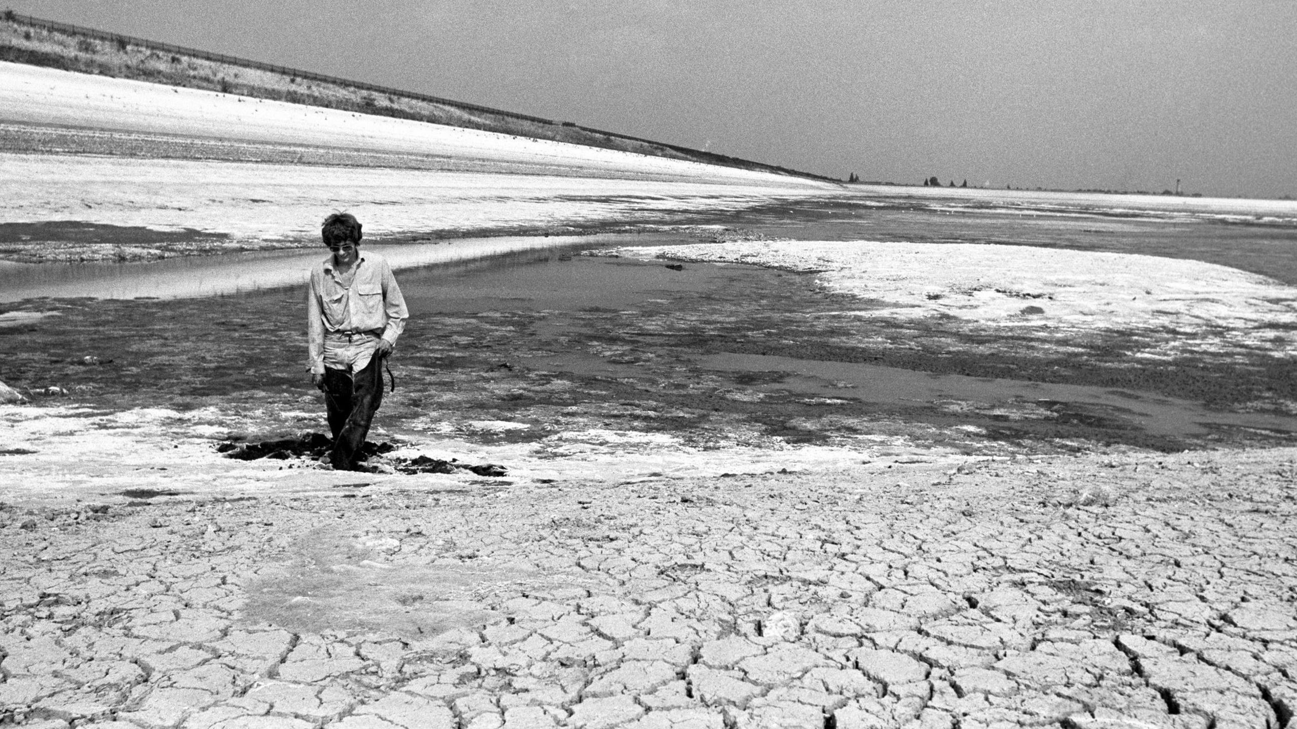 Man walks through mud in dried and cracked reservoir bed