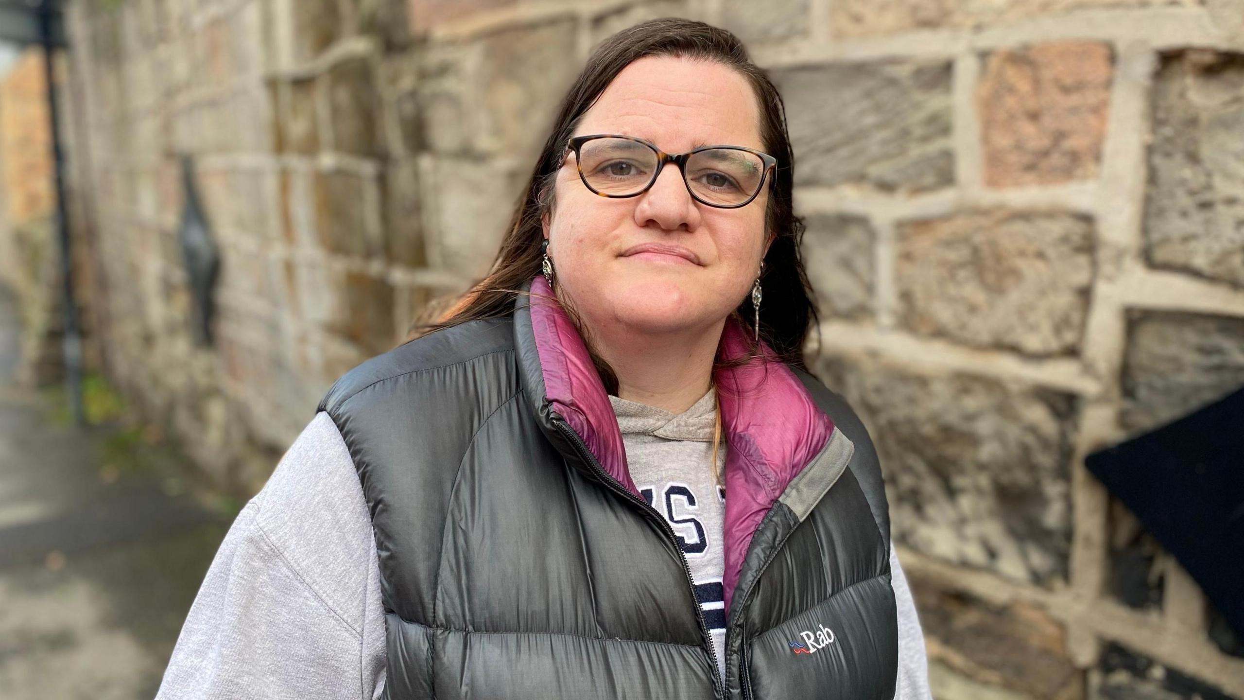 An image of a woman, with brown hair and glasses, wearing a gilet jacket