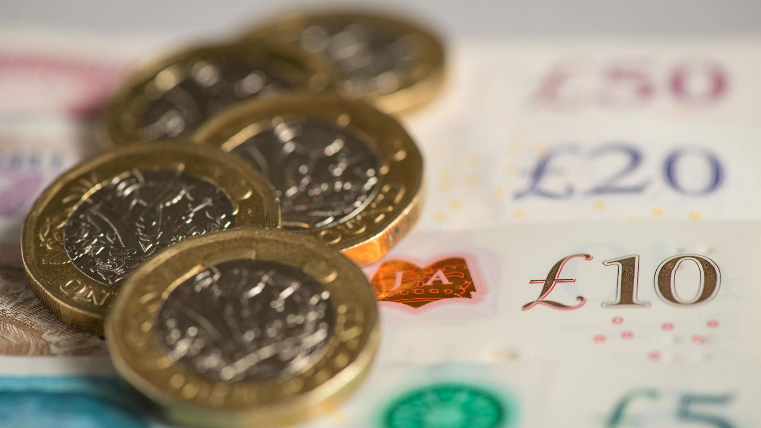 Pound coins sitting on top of £5, £10, £20 and £50 notes