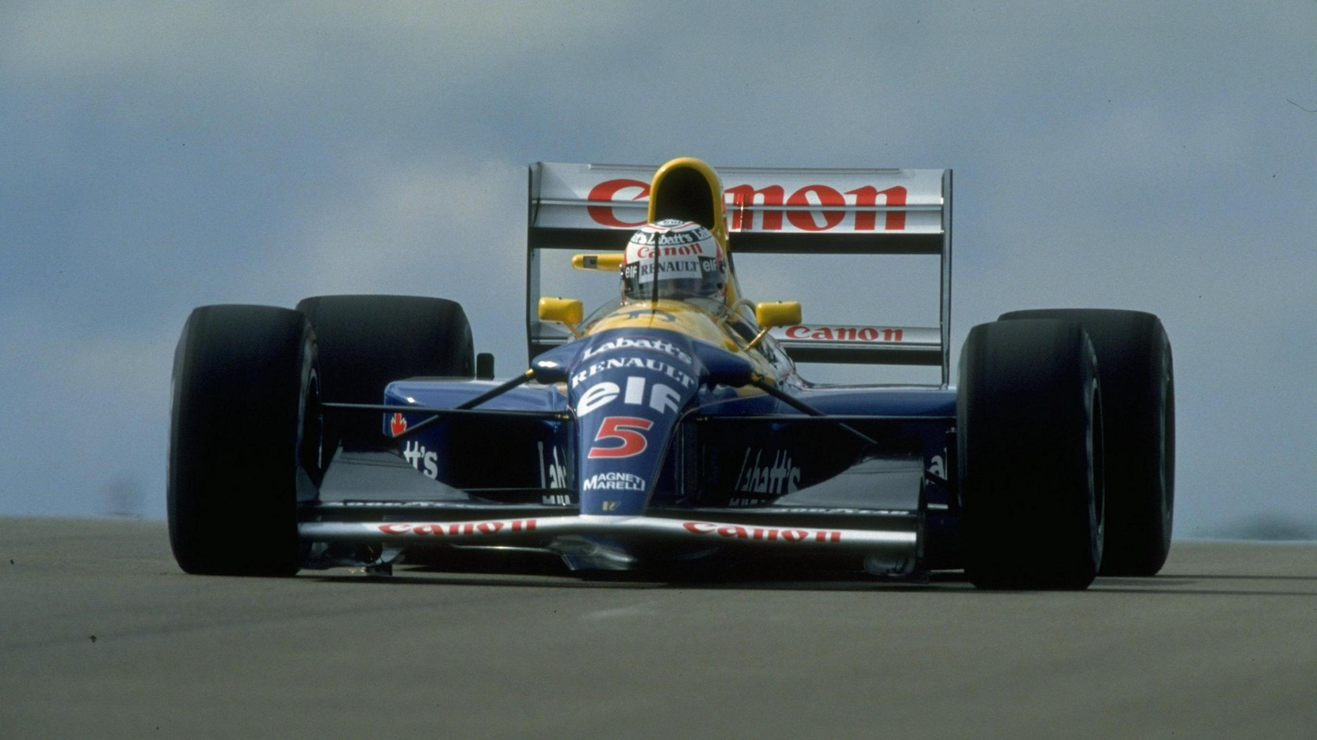 Racing car mid-circuit with a blue body, with the words Renault Elf 4 on the front. The word Canon appears on the rear wing in red writing. Nigel Mansell's helmet is visible protruding from the cockpit. The car has very large black tyres.