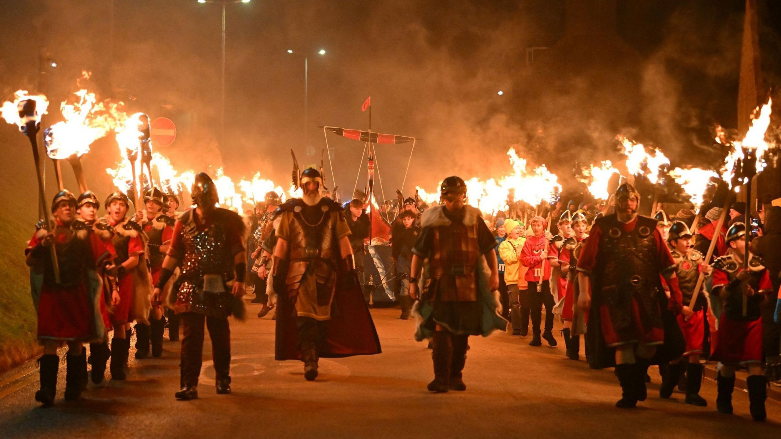People, some of them dressed in Viking-like outfits, march through the night carrying burning torches.