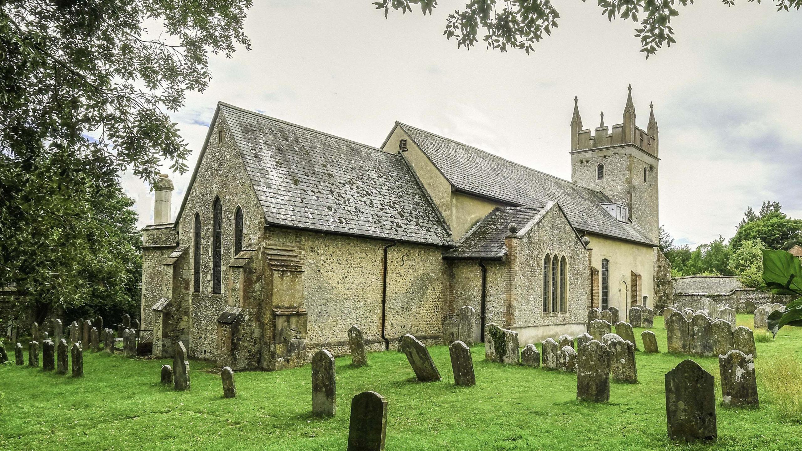 A large grey stone church and grassy graveayard