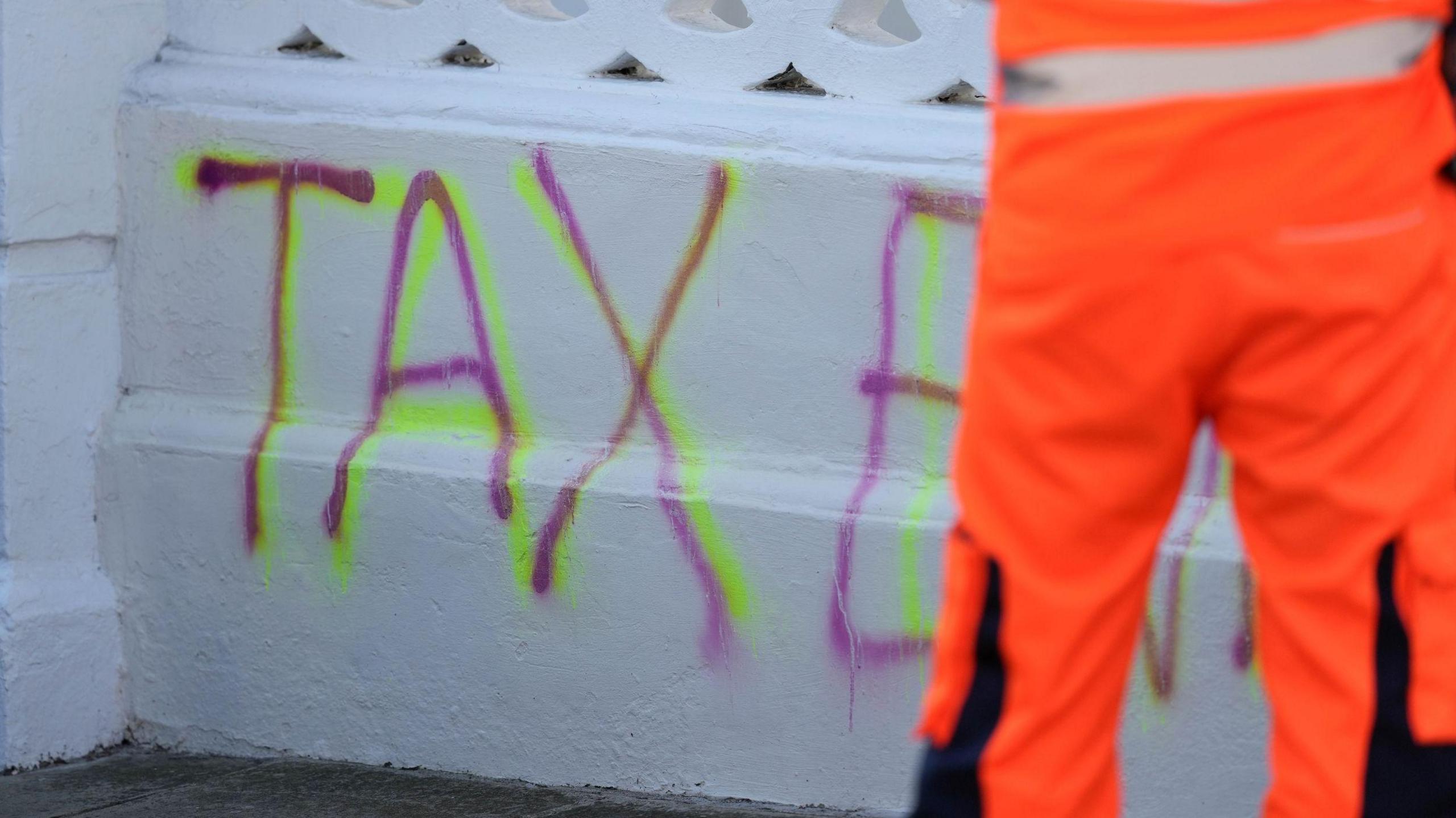 A white wall outside a house with the word "tax evasion" wrote in pink on it