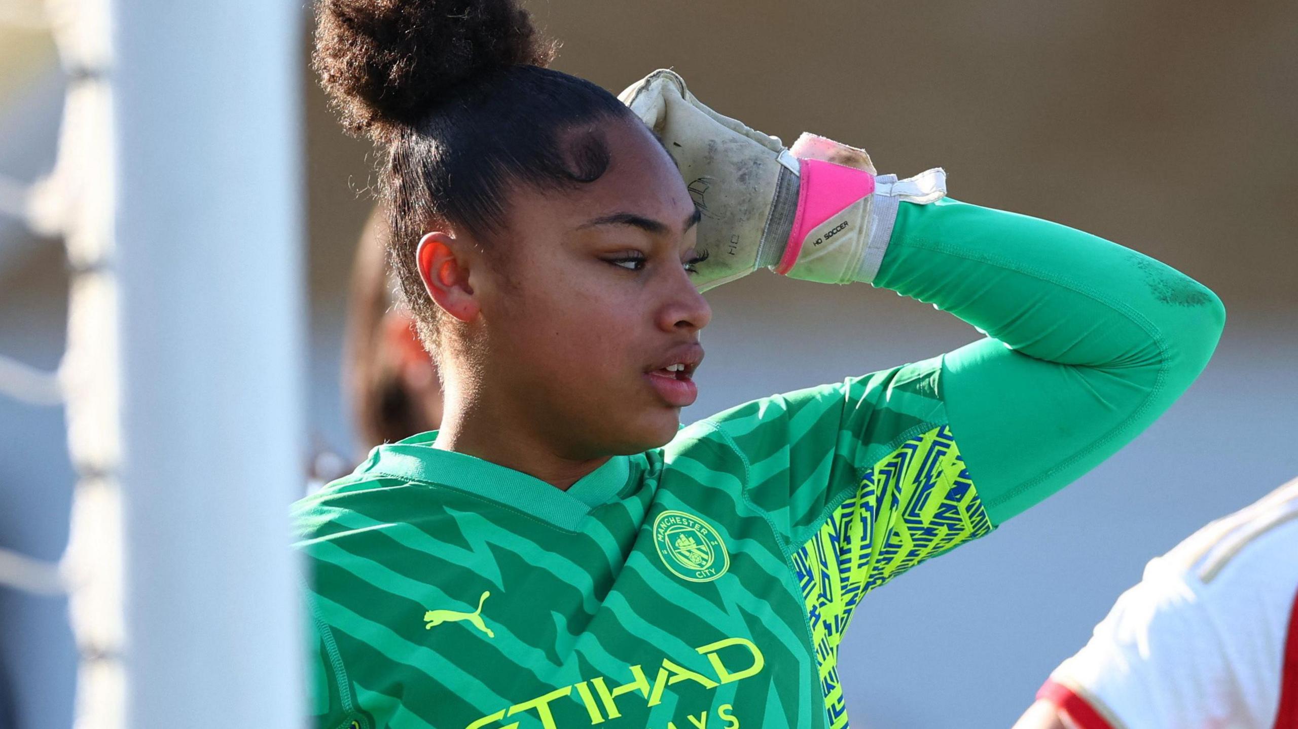 Manchester City goalkeeper Khiara Keating, with black hair scraped into a bun, wearing a dark and light green goalkeeper's shirt and white  gloves with a pink wristband