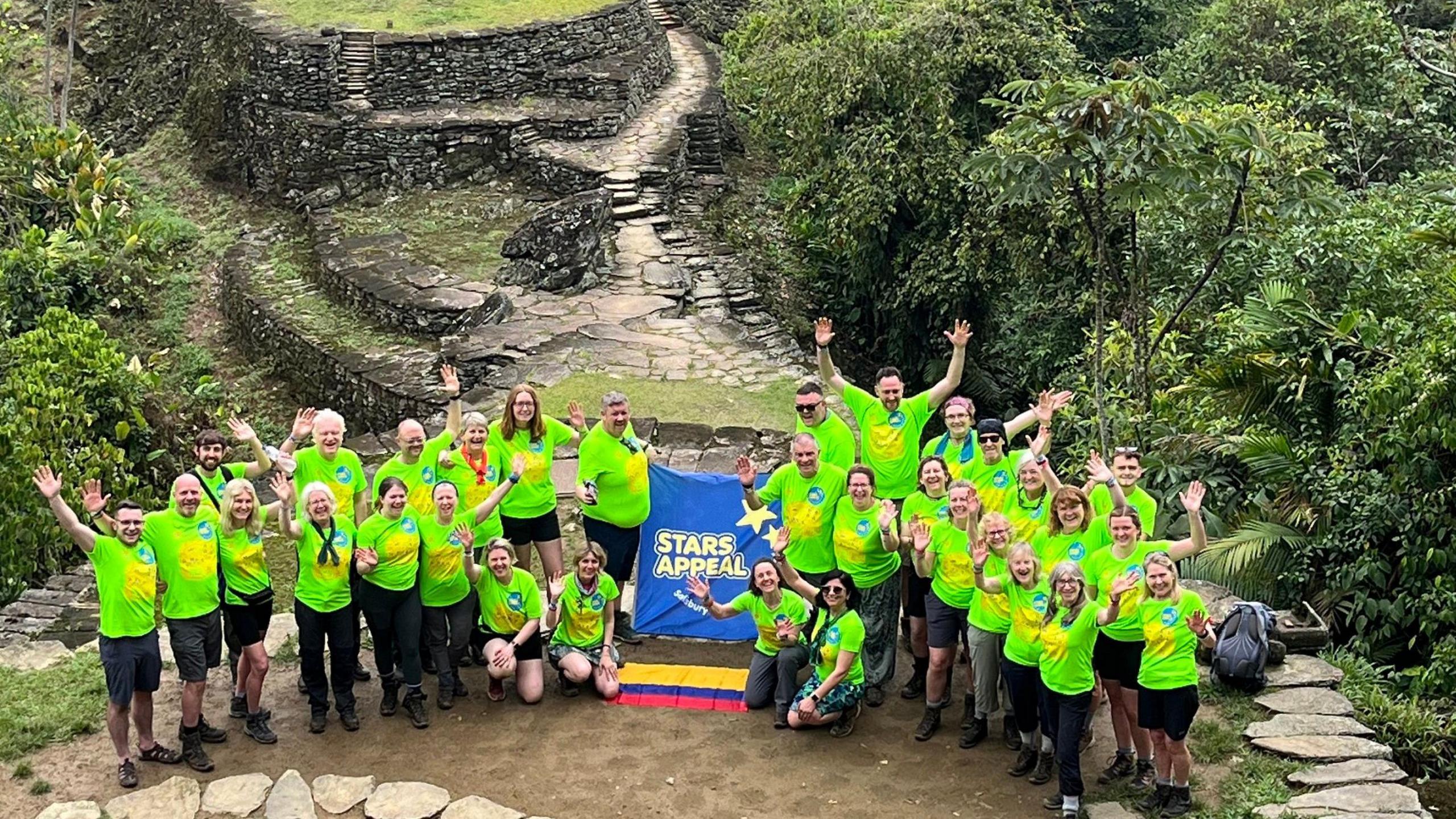 Group of people in fluorescent green t shirts atop a mountain with a banner saying 'Stars Appeal' and a Columbian flag