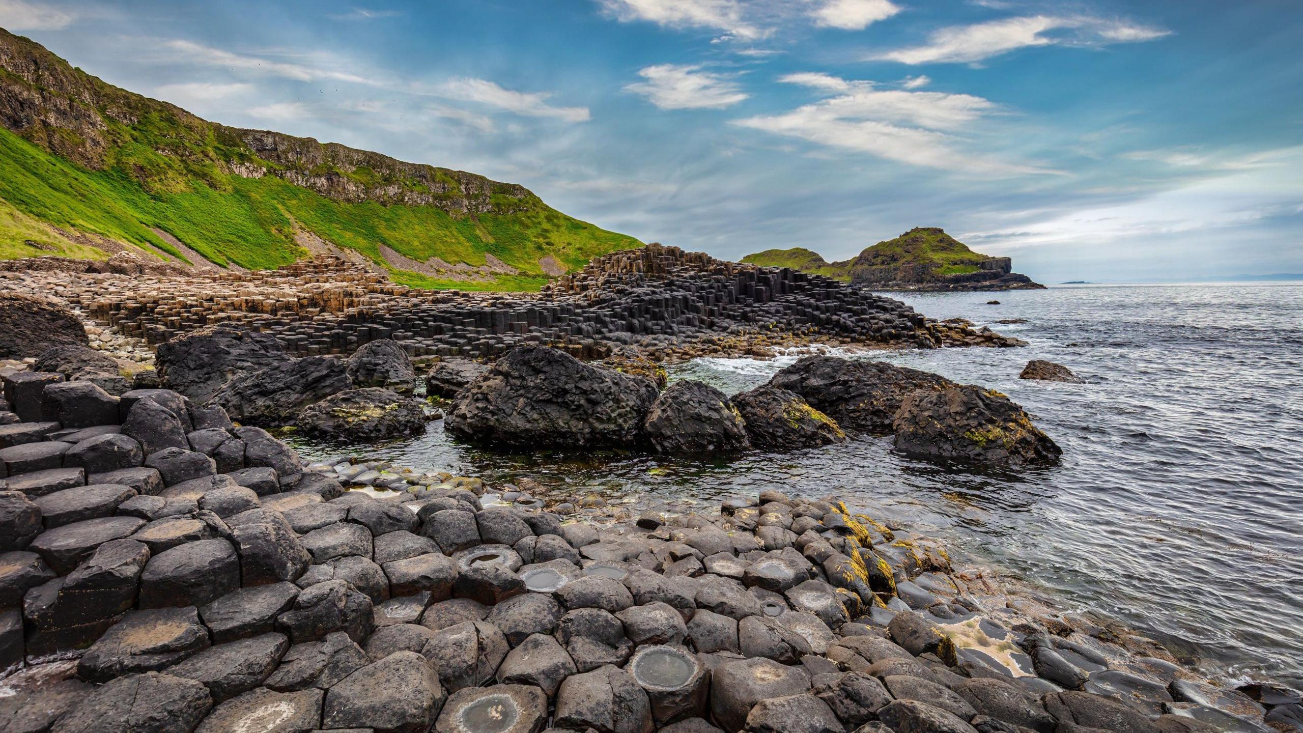 The volcanic stones that make up the giants causeway, seen on a sunny bright day, with the sea on one side and rolling hills on the other