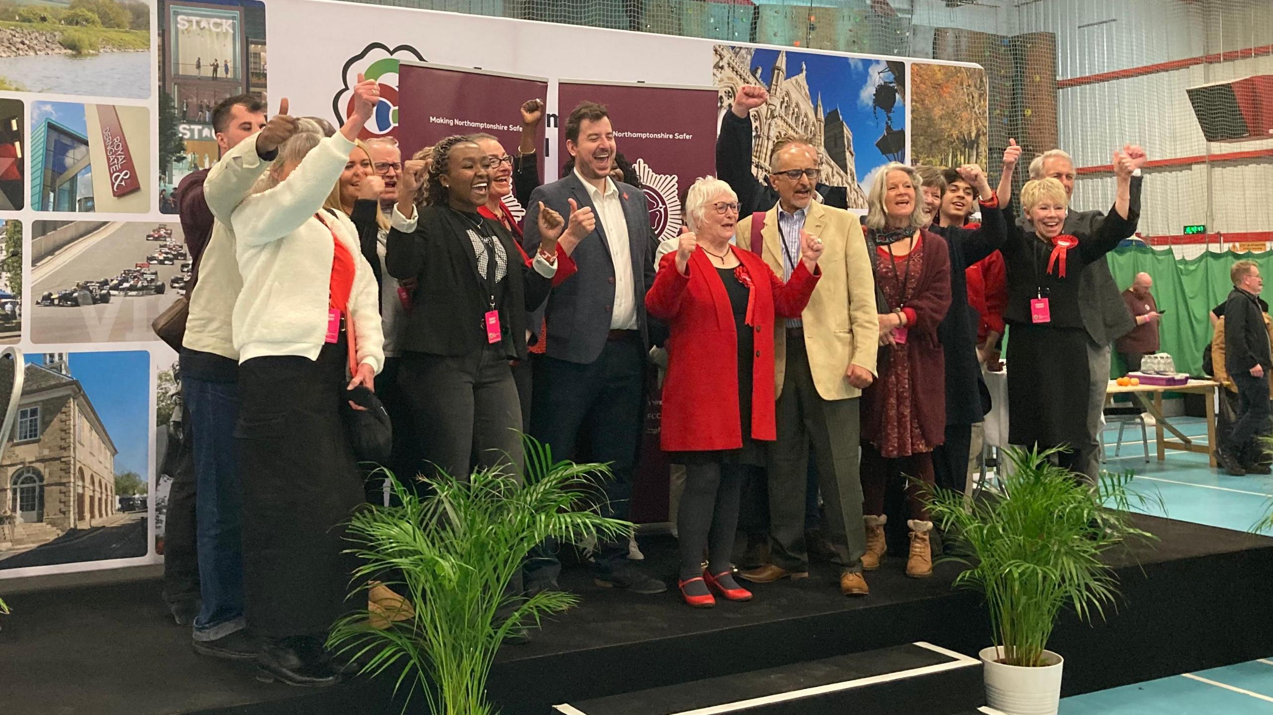 Group of people on a stage with Danielle Stone leading a cheer