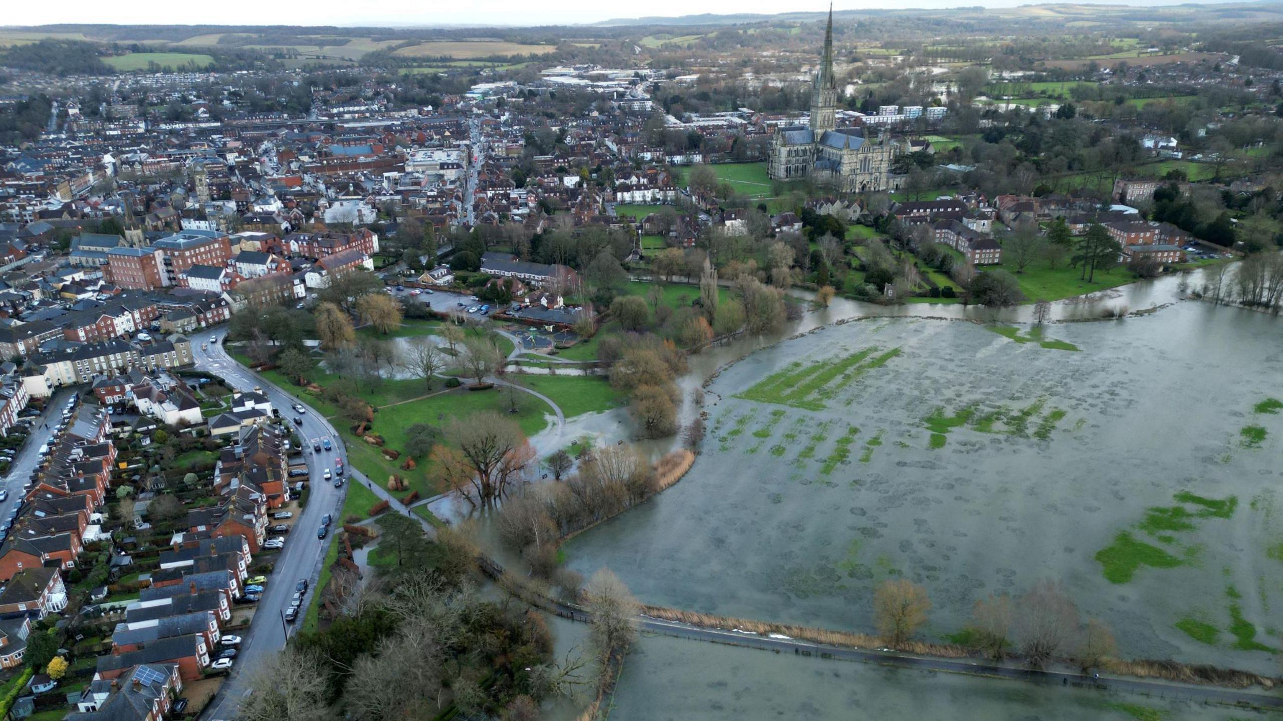 An aerial view of Salisbury showing fields on the edge of the city under flood water. The famous cathedral and the city centre are visible in the background