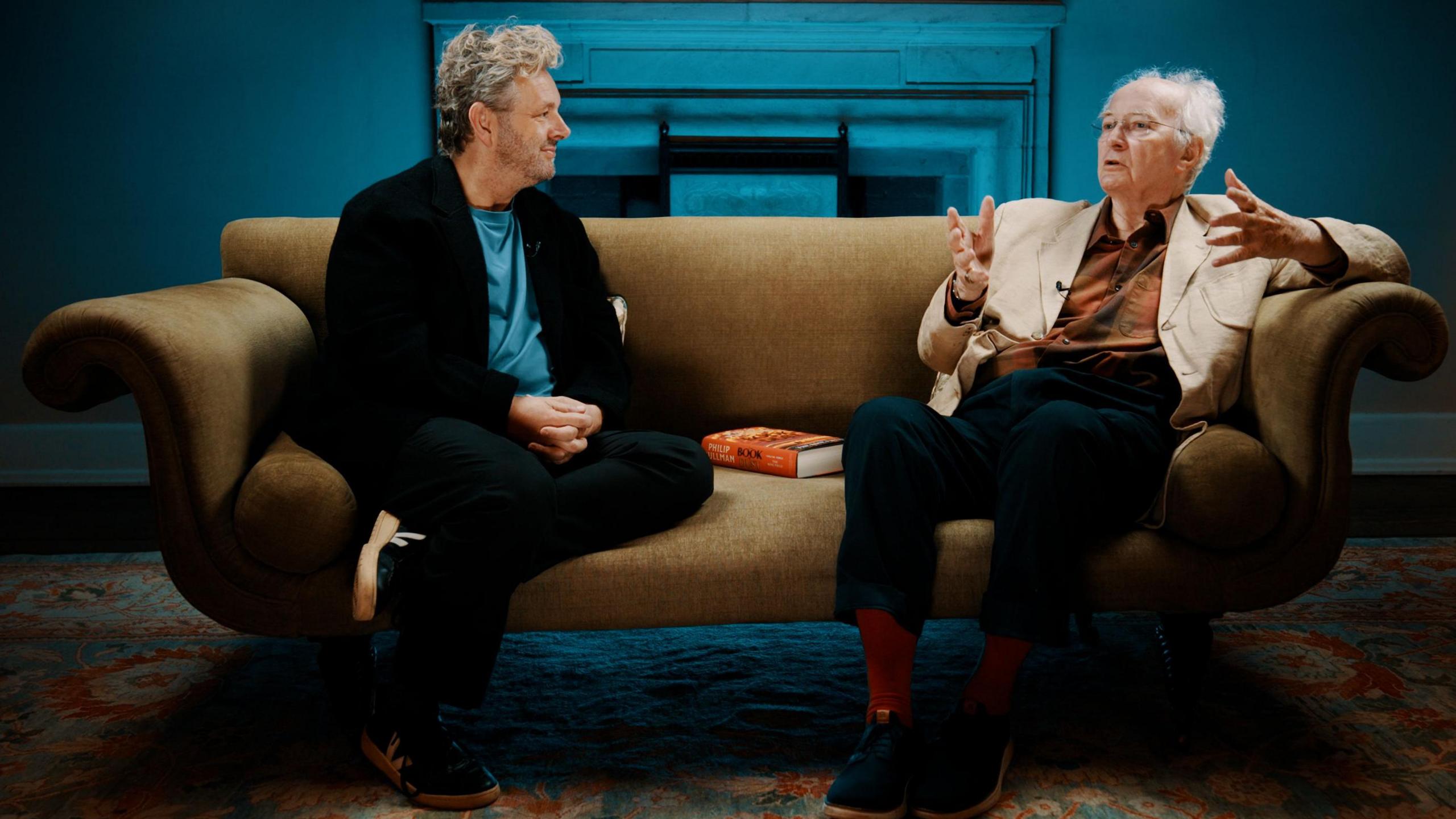 Michael Sheen and Philip Pullman talking on a sofa